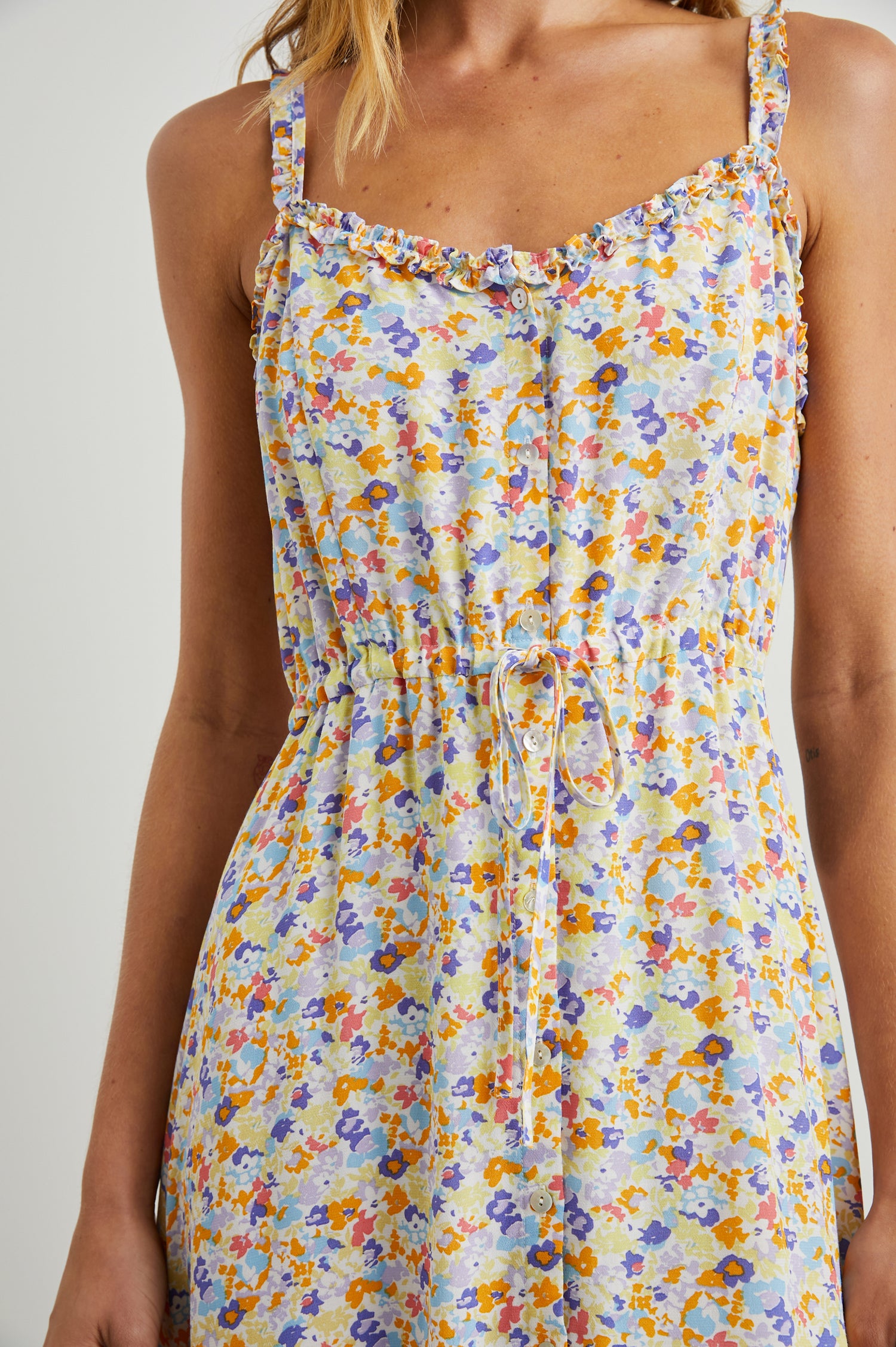 Adalyn Sleeveless Midi Dress with Thin Shoulder Straps, Buttons Down the Front, a Drawstring Waist, a Ruffled Hem and Ruffled Trim in Papaya Flowers Colorway, Purples, Blue, Yellow and Orange on White - Front View Featured on Model 