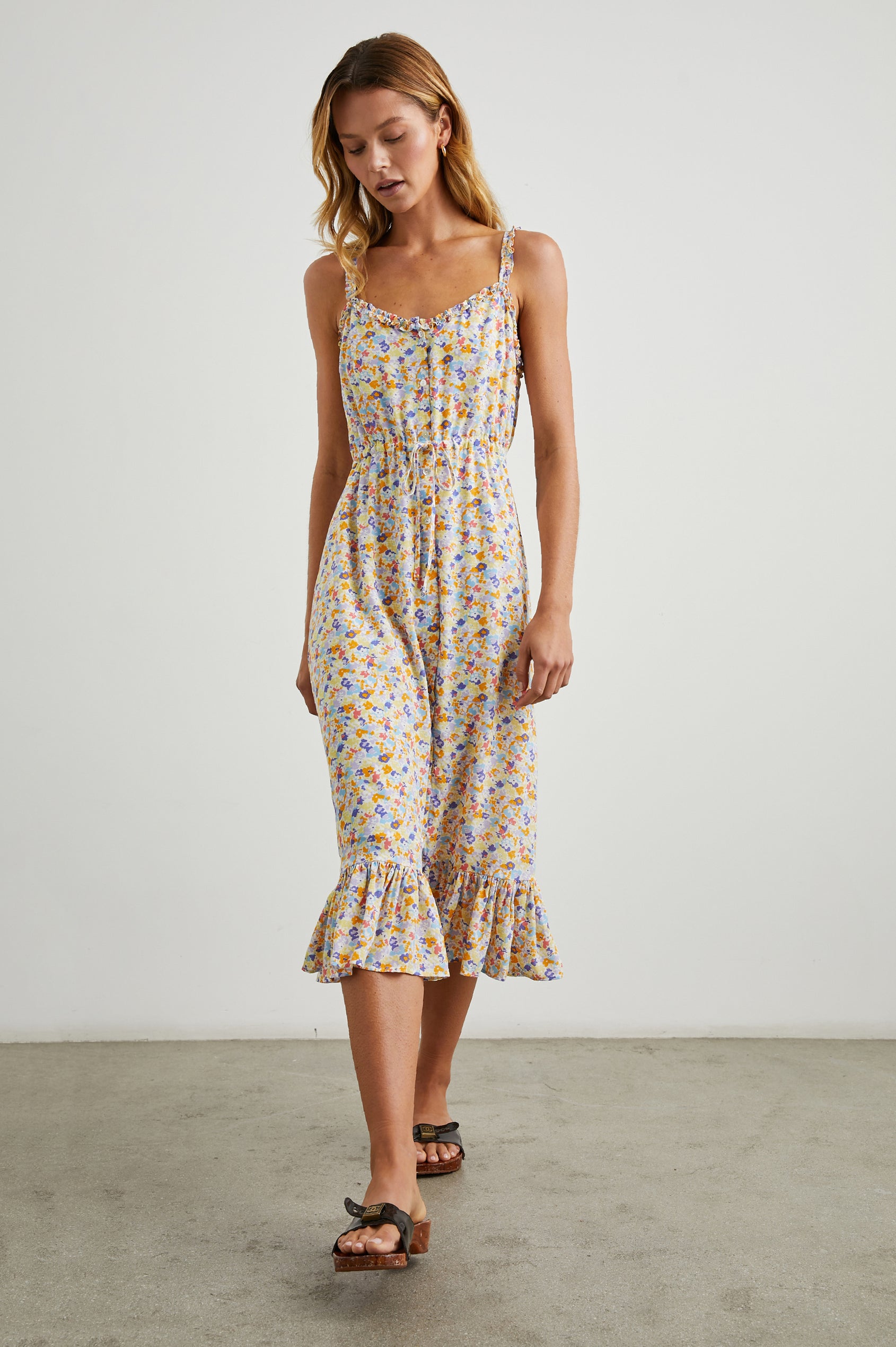 Adalyn Sleeveless Midi Dress with Thin Shoulder Straps, Buttons Down the Front, a Drawstring Waist, a Ruffled Hem and Ruffled Trim in Papaya Flowers Colorway, Purples, Blue, Yellow and Orange on White - Front Full Body View Featured on Model 