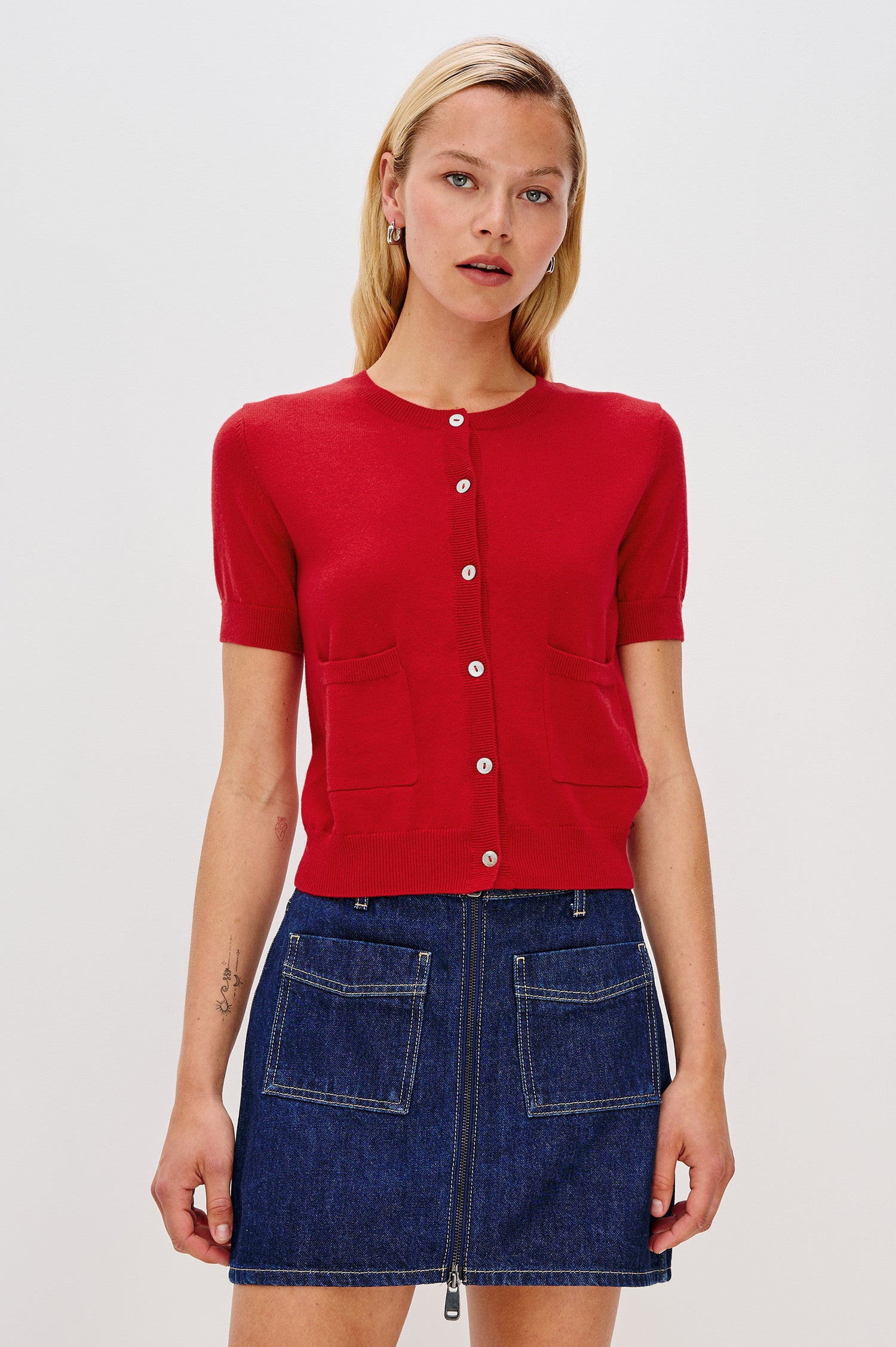 Aisley short-sleeved, bright Crimson red knit cardigan featuring white buttons, a round neckline, and two small front pockets - front view featured on model.