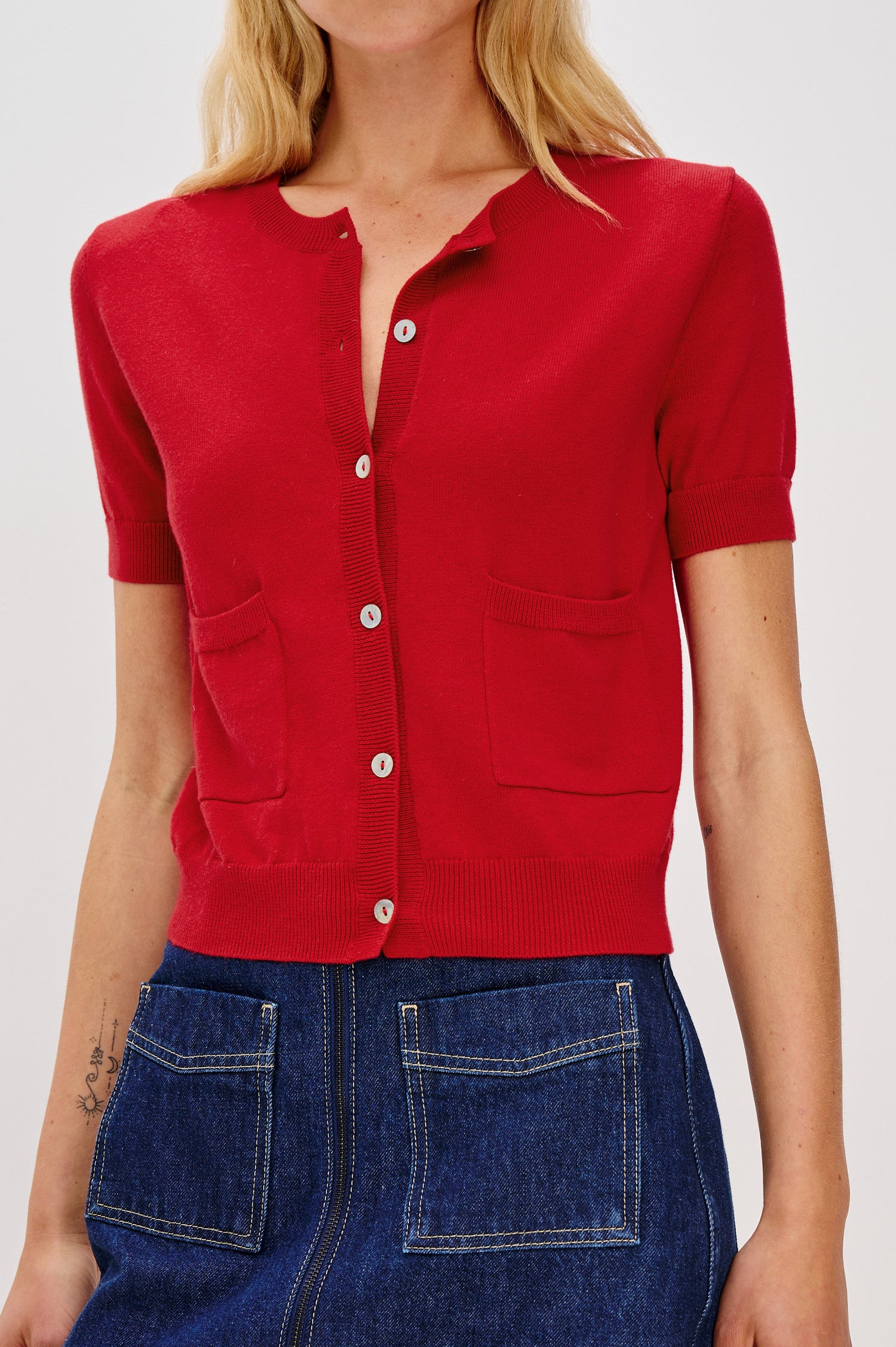 Aisley short-sleeved, bright Crimson red knit cardigan featuring white buttons, a round neckline, and two small front pockets - front view featured on model.