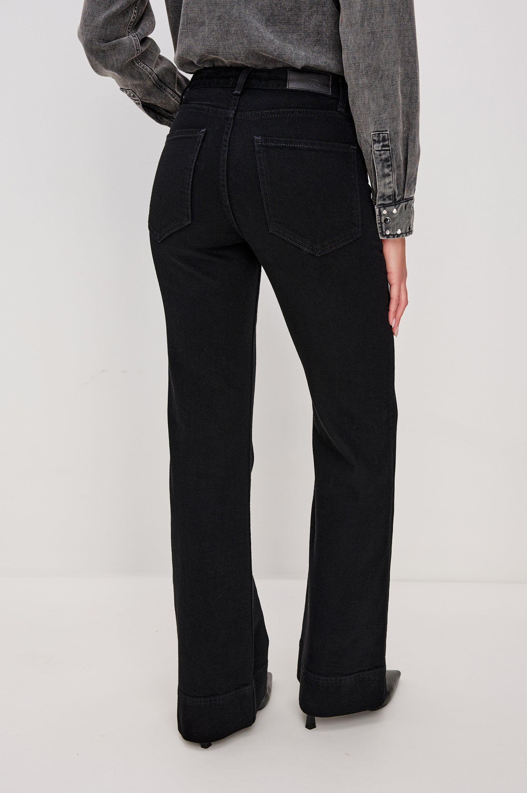Alamitos is a high waisted denim trouser with flared leg and front patch pockets in Blackout colorway. Back full body view featured on model.