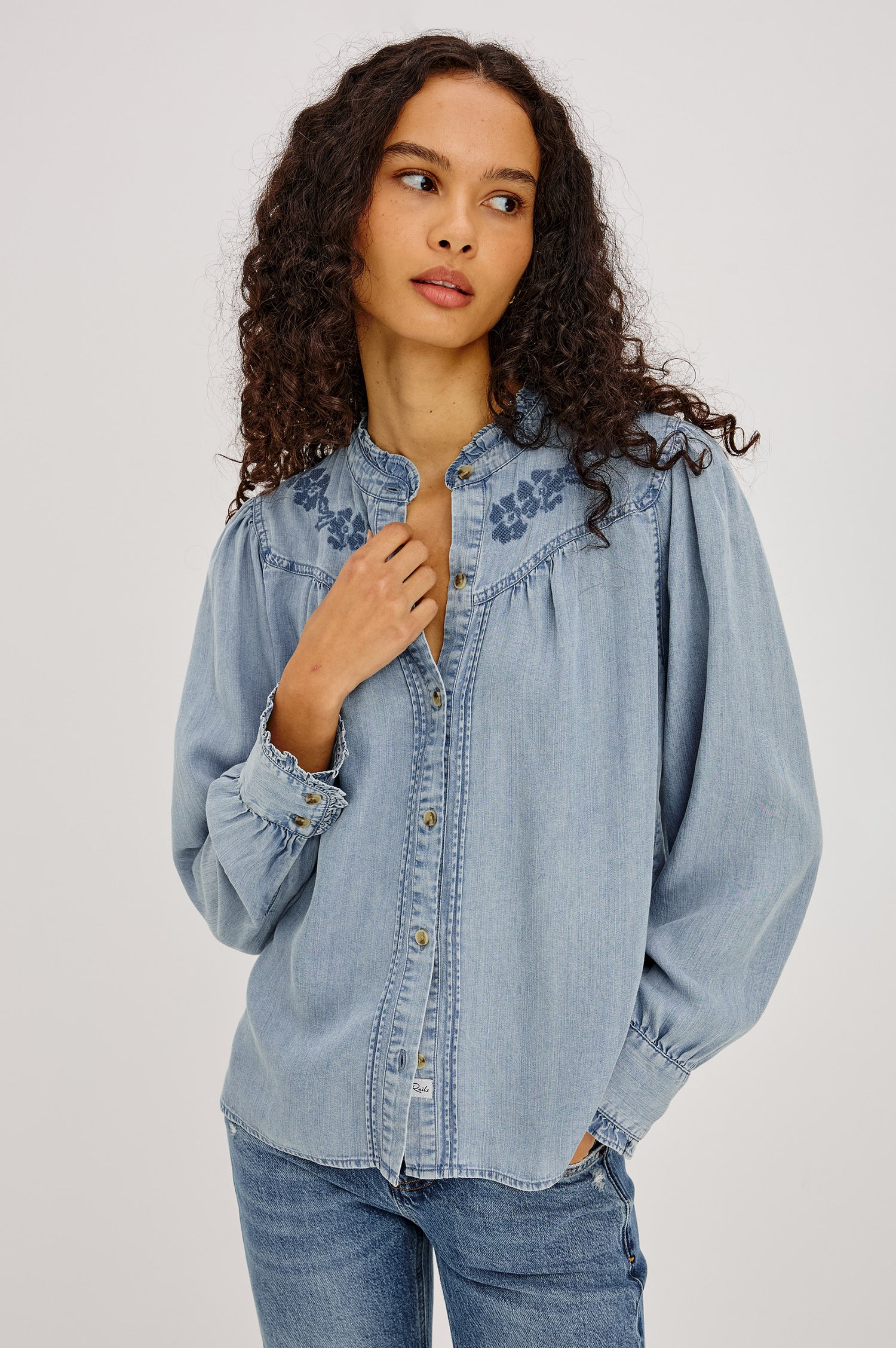 Alanna Shirt in TENCEL™ Denim With Front Buttons, Relaxed Fit, Pointelle Floral Embroidery, Long Sleeves, Curved Yoke, and Ruffle Trim in Medium Cloud Wash Colorway - Upper Body Front View Featured on Model