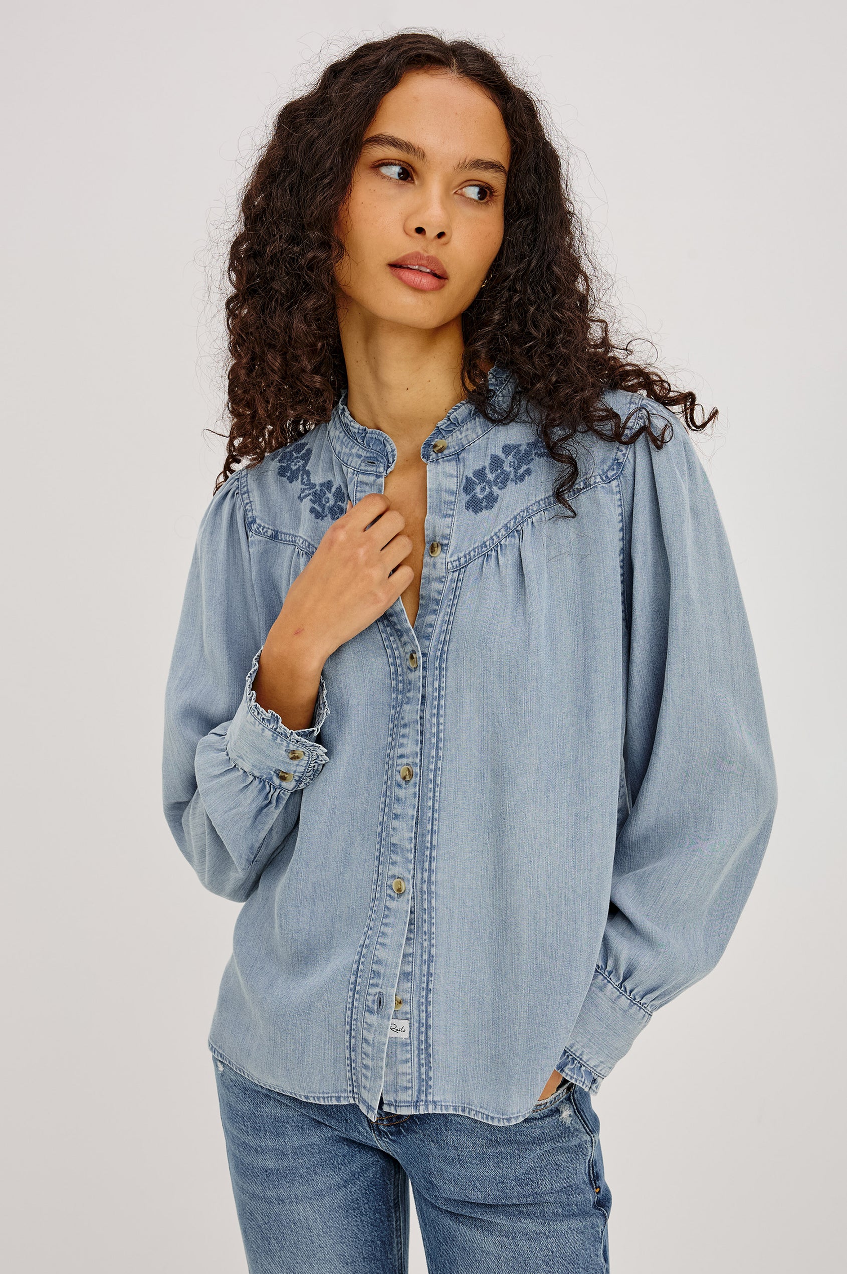Alanna Shirt in TENCEL™ Denim With Front Buttons, Relaxed Fit, Pointelle Floral Embroidery, Long Sleeves, Curved Yoke, and Ruffle Trim in Medium Cloud Wash Colorway - Upper Body Front View Featured on Model