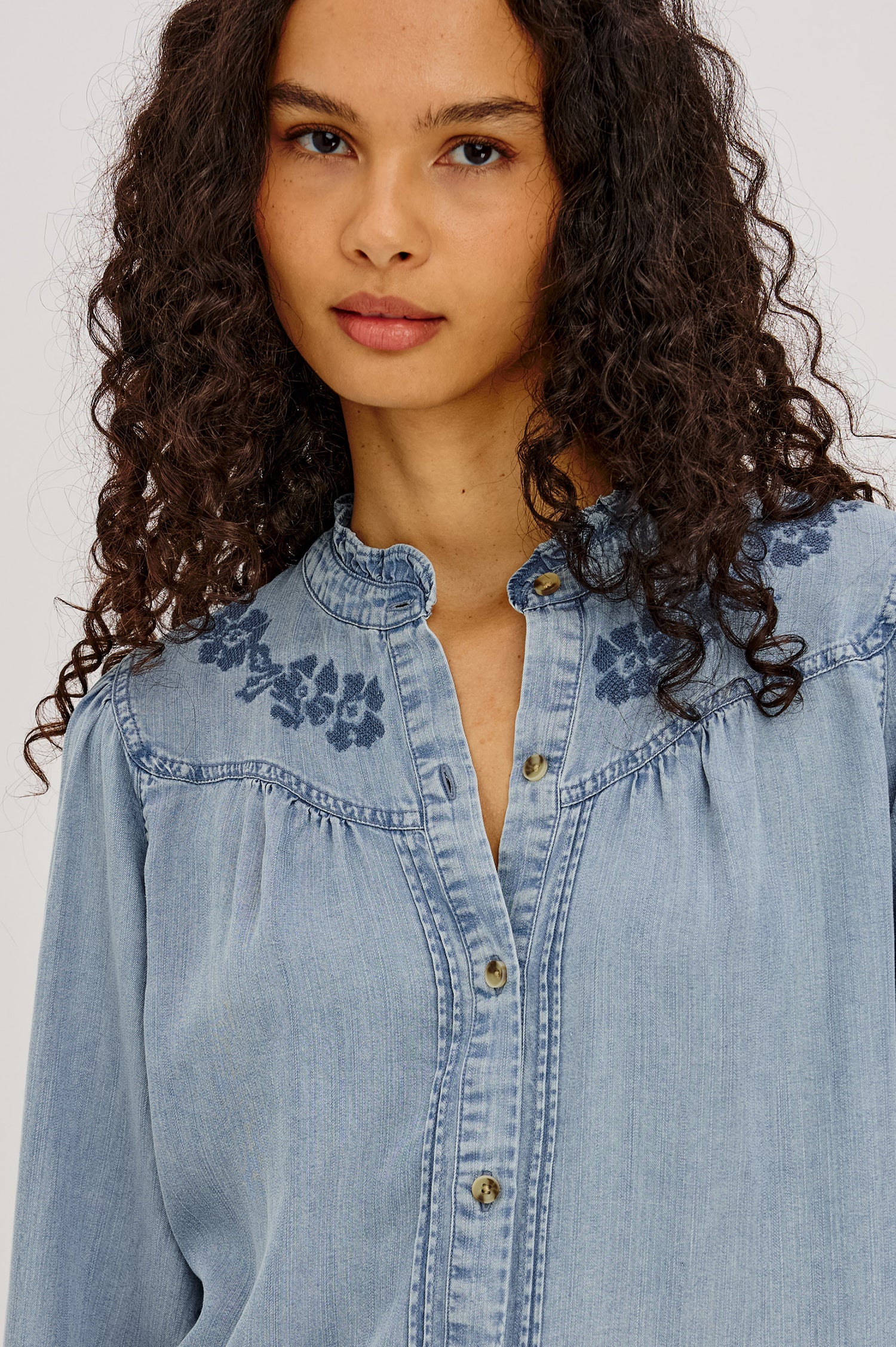 Alanna Shirt in TENCEL™ Denim With Front Buttons, Relaxed Fit, Pointelle Floral Embroidery, Long Sleeves, Curved Yoke, and Ruffle Trim in Medium Cloud Wash Colorway - Upper Body Front View Featured on Model