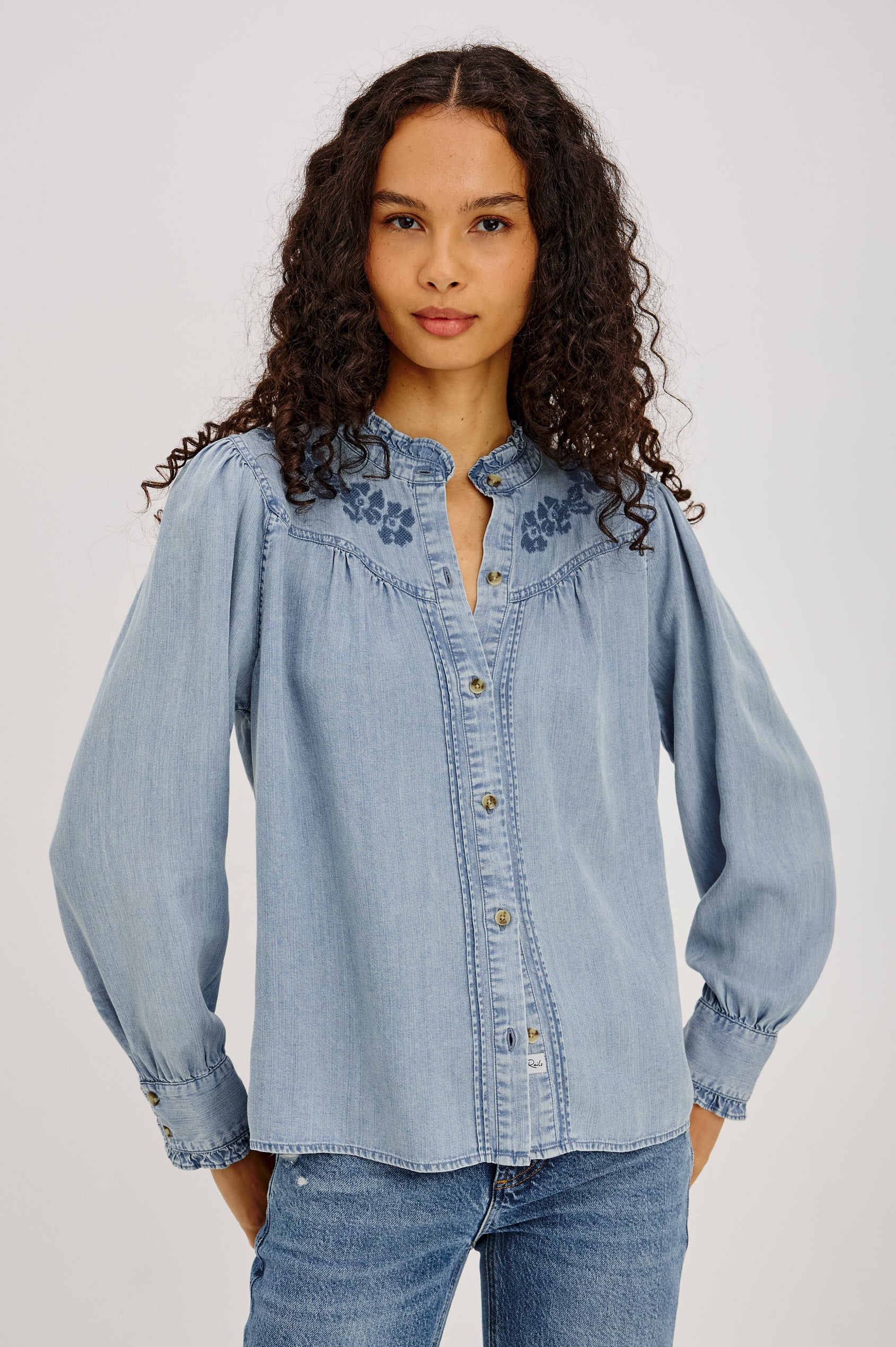 Alanna Shirt in TENCEL™ Denim With Front Buttons, Relaxed Fit, Pointelle Floral Embroidery, Long Sleeves, Curved Yoke, and Ruffle Trim in Medium Cloud Wash Colorway - Upper Body Front View Featured on Model