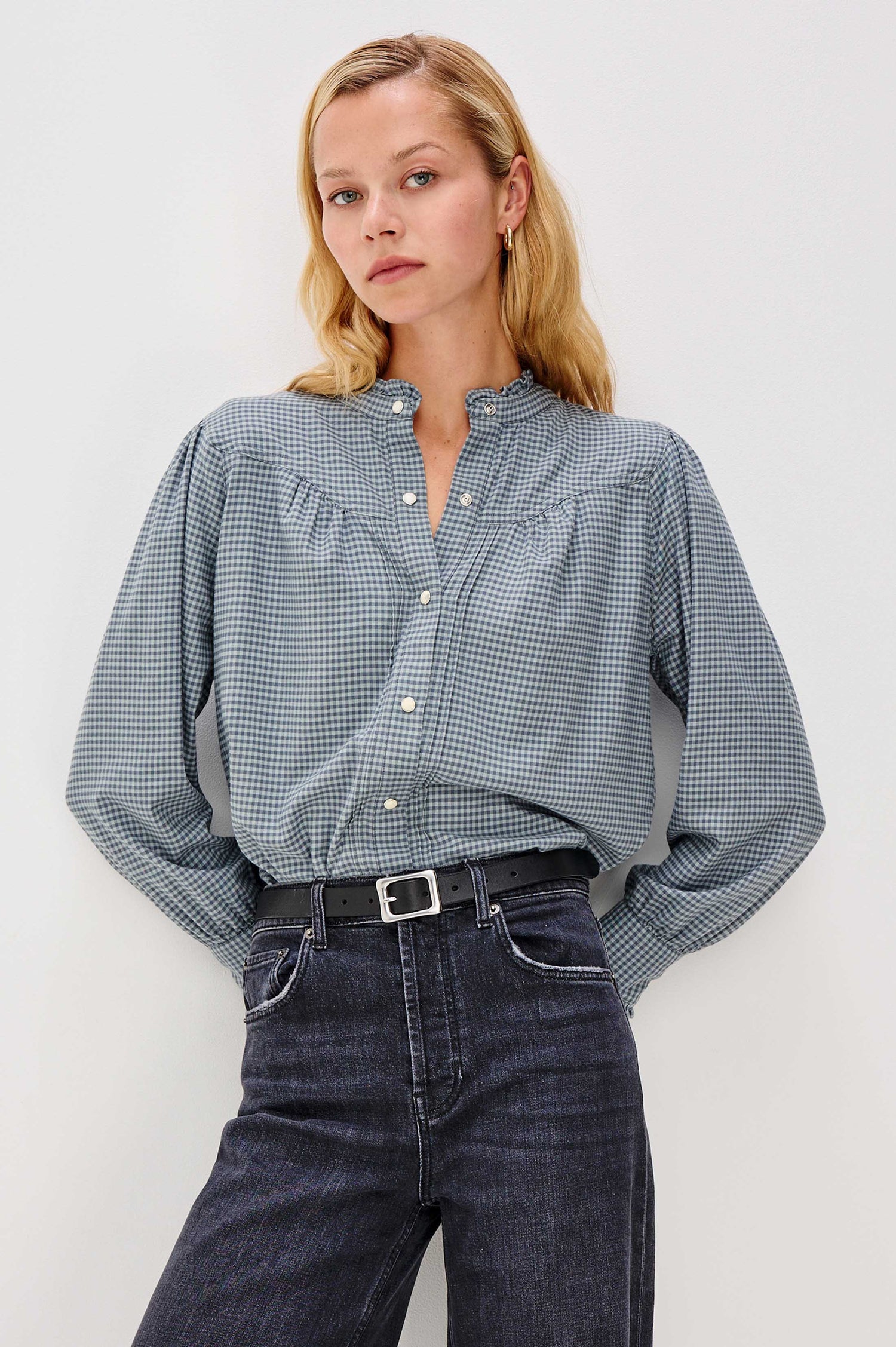 Woman wearing a blue checkered blouse and dark jeans against a white background