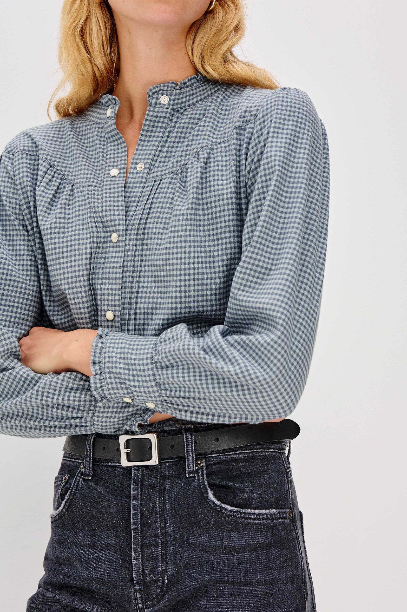 Person wearing a blue checkered shirt and dark jeans on a light gray background