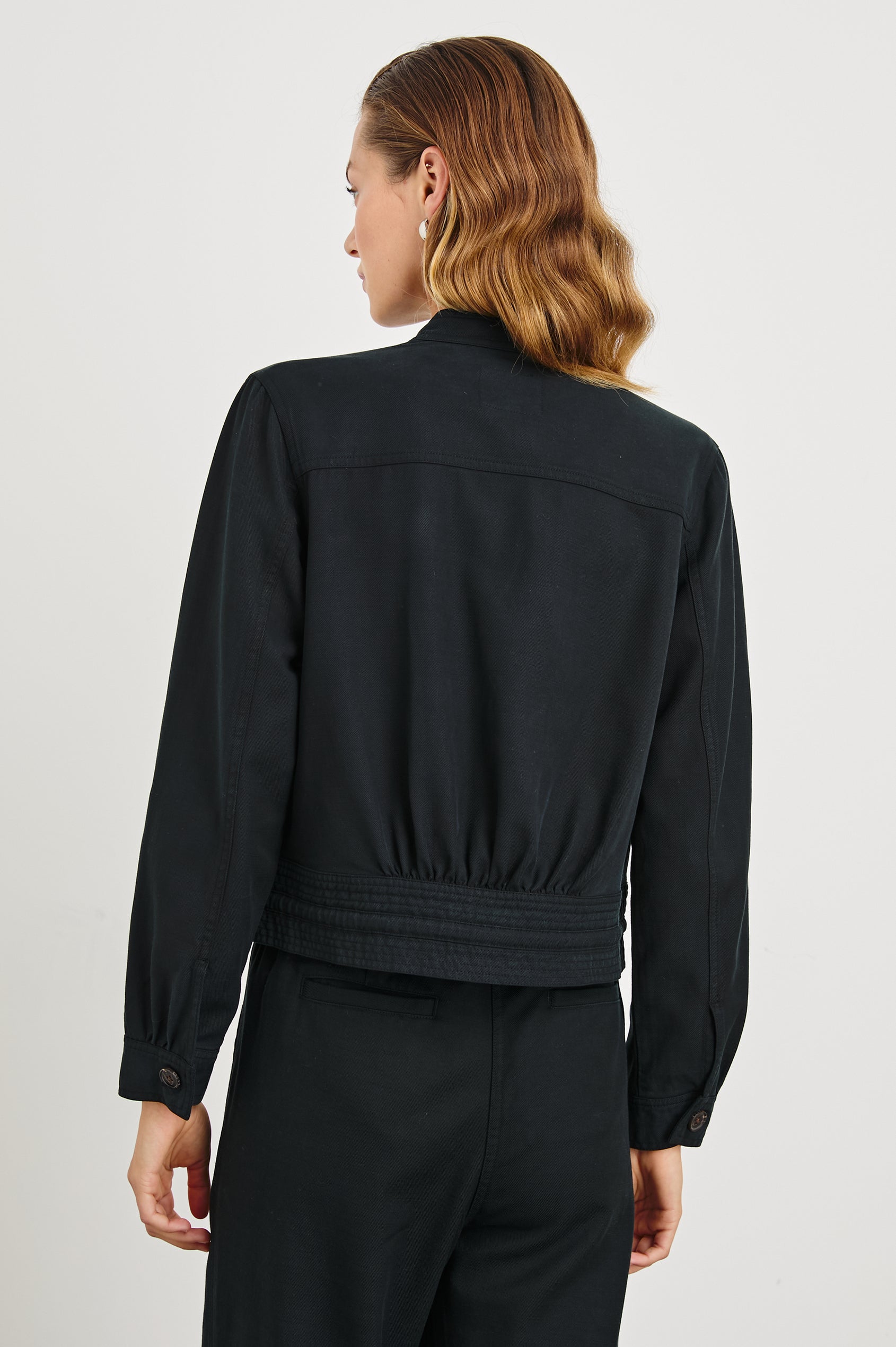 Alma Jacket with Button Closure, Mandarin Collar, Two Large Chest Button Patch Pockets and a Drawcord at the Hem in Black Colorway - Back View Featured on Model