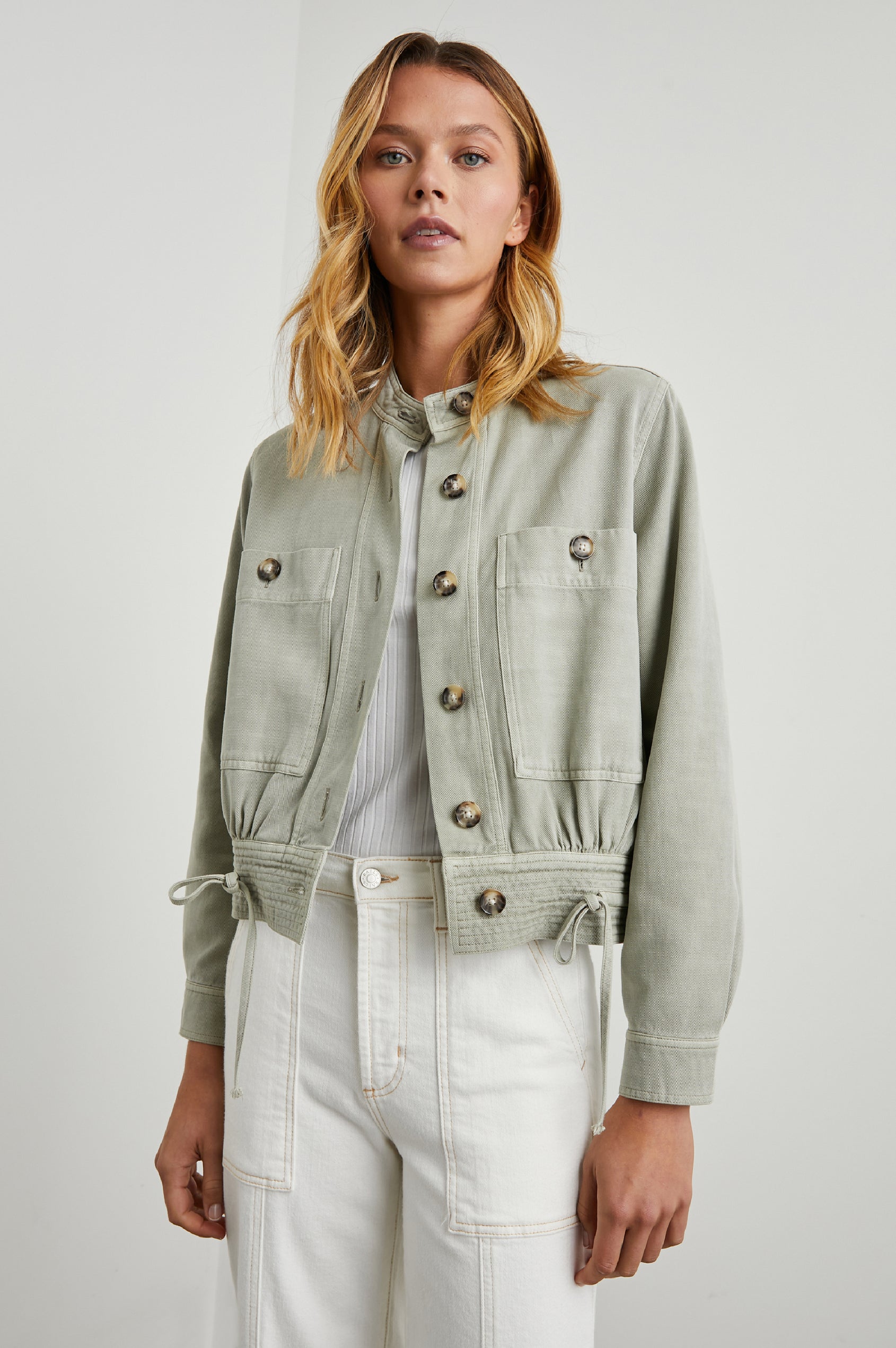 Alma Jacket with Button Closure, Mandarin Collar, Two Large Chest Button Patch Pockets and a Drawcord at the Hem in Sage Colorway - Front View Featured on Model