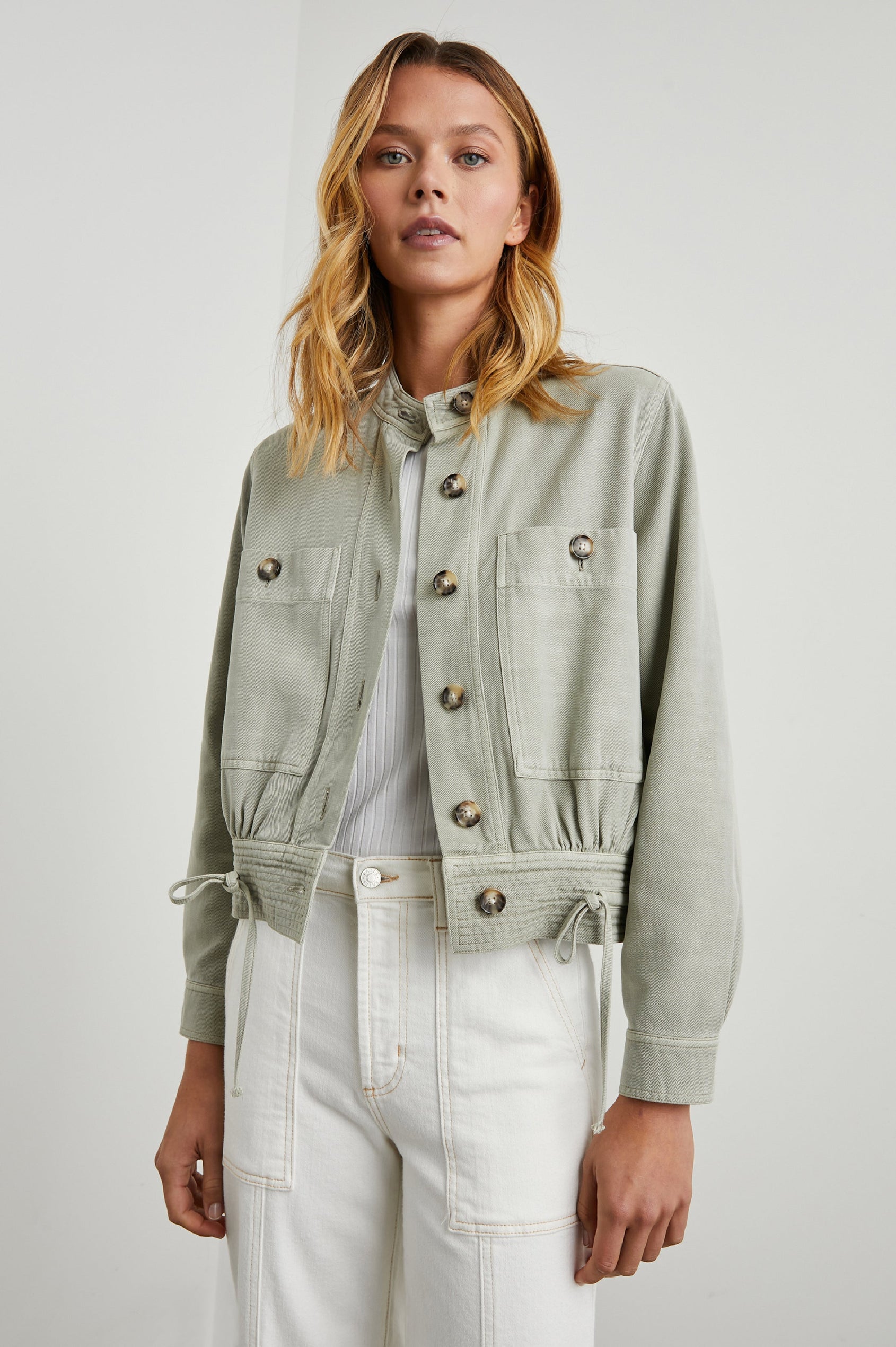 Alma Jacket with Button Closure, Mandarin Collar, Two Large Chest Button Patch Pockets and a Drawcord at the Hem in Sage Colorway - Front View Featured on Model