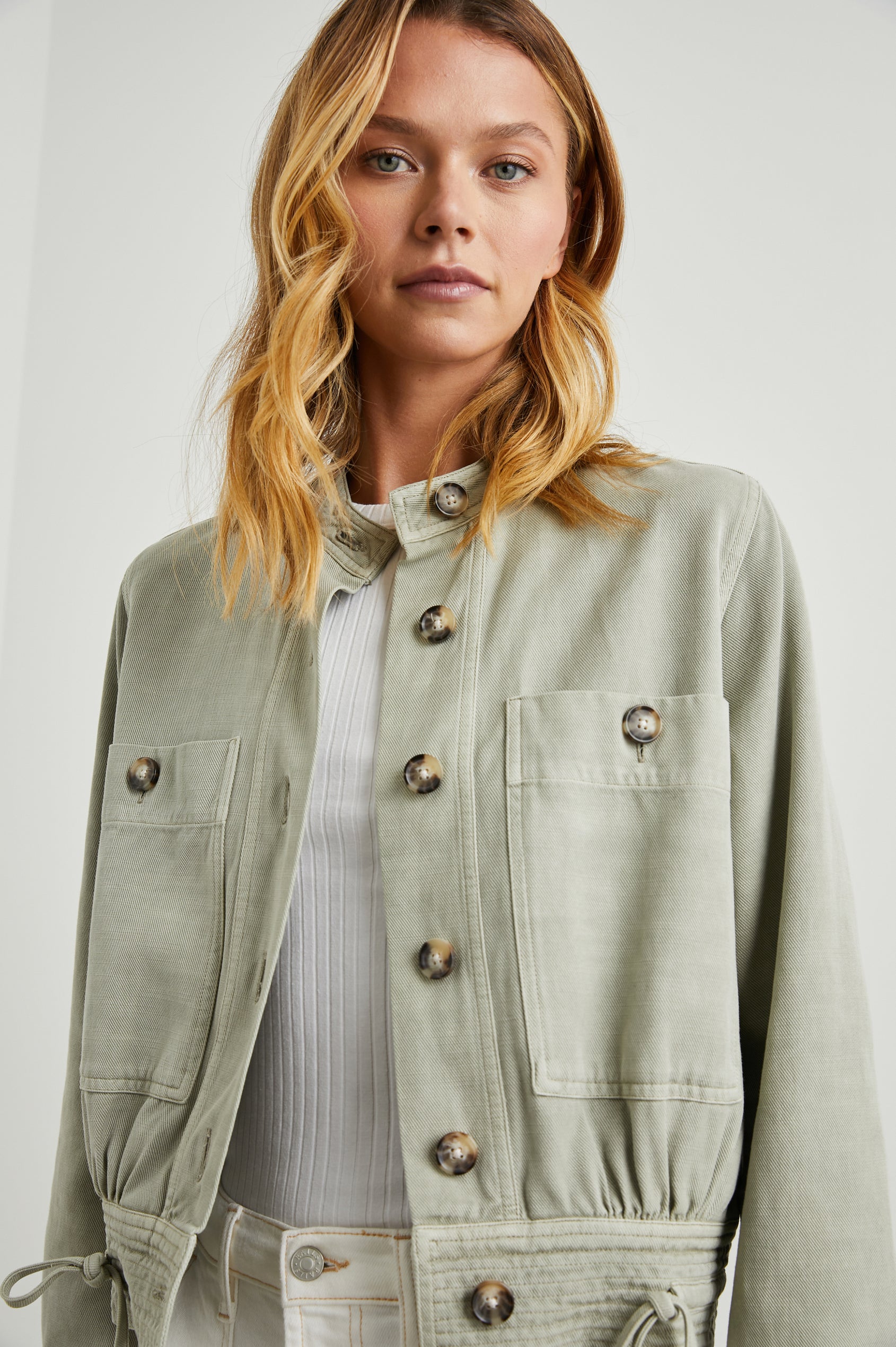 Alma Jacket with Button Closure, Mandarin Collar, Two Large Chest Button Patch Pockets and a Drawcord at the Hem in Sage Colorway - Front View Featured on Model