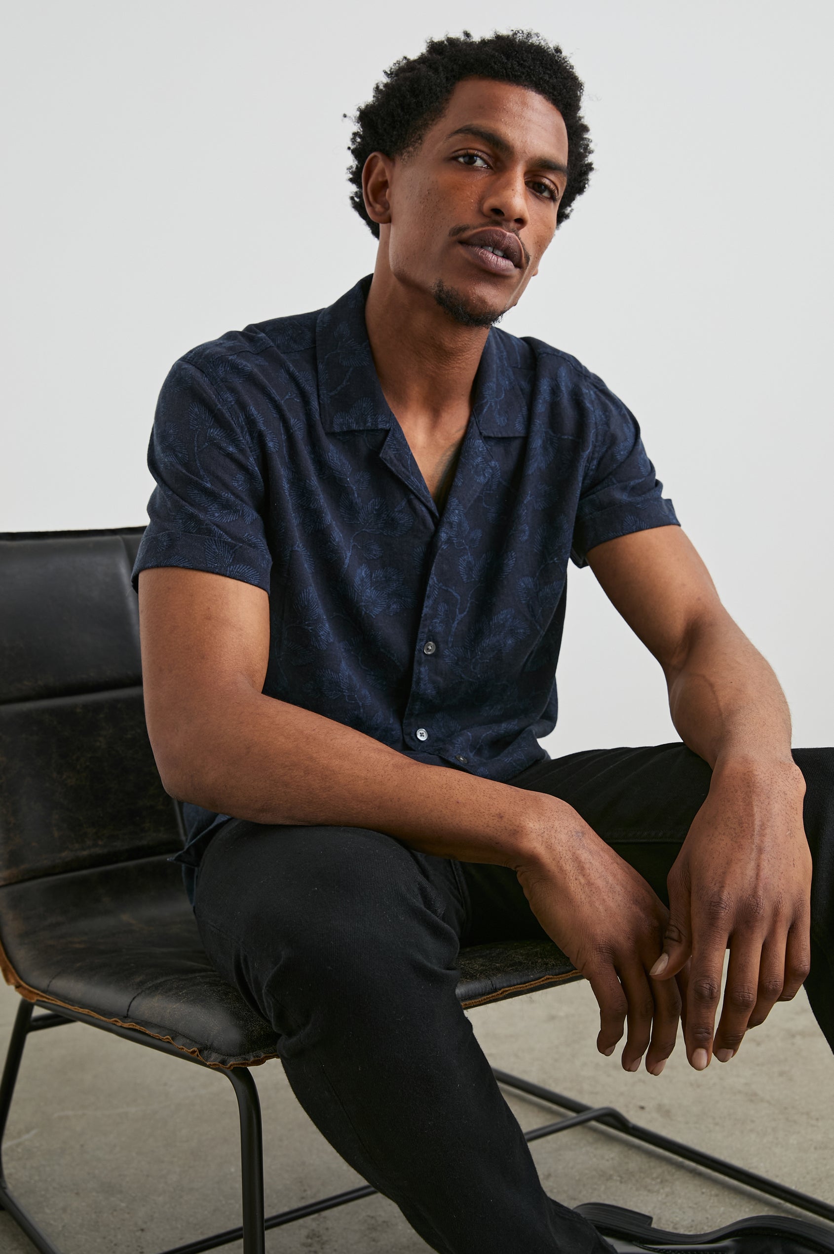 Amalfi Short-Sleeve Button Up in Japanese Maple Indigo Colorway, Indigo leaves on Black  - Front View Featured on Seated Model