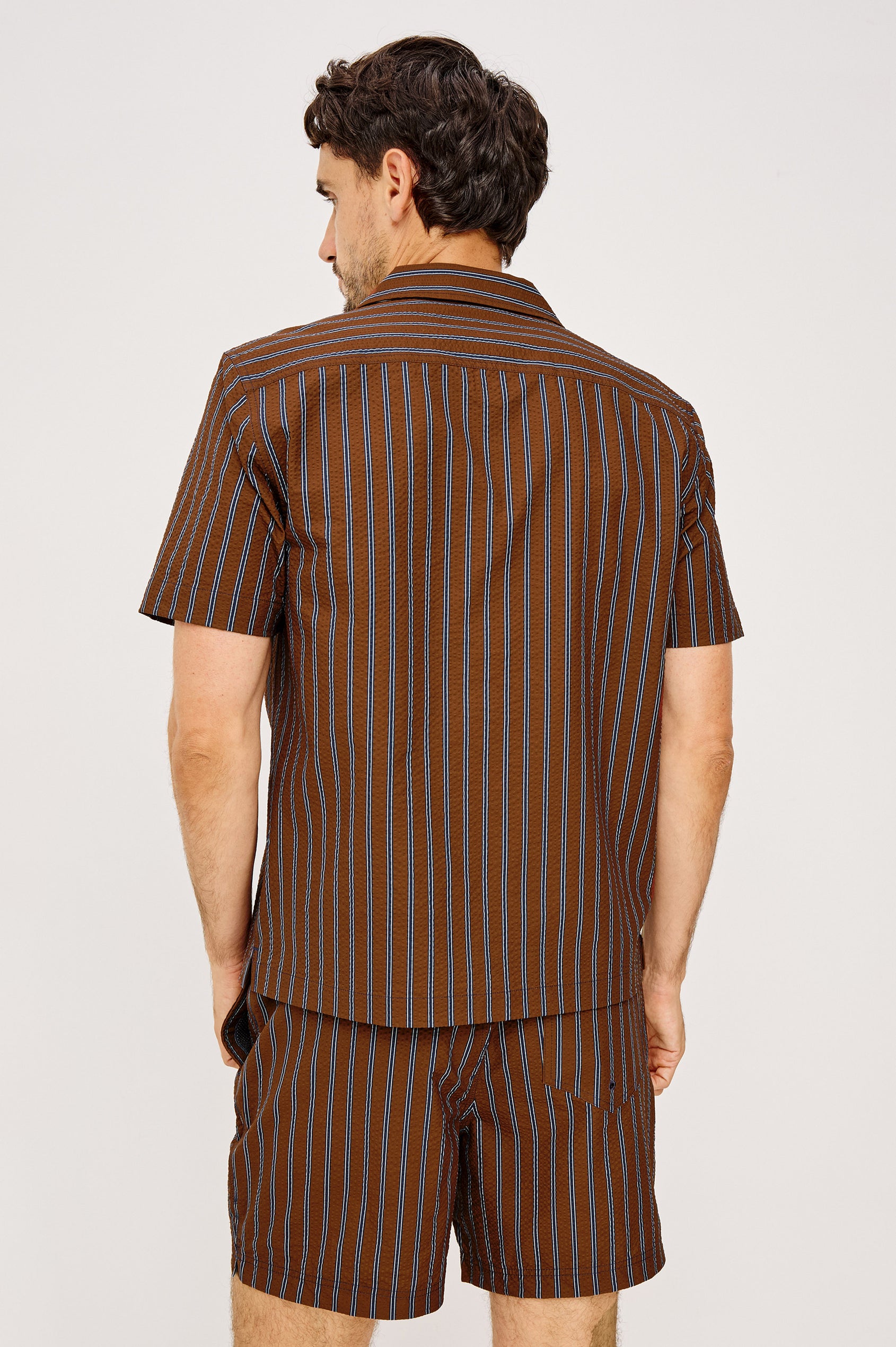 Amalfi Camp Shirt in Lightweight Seersucker With Notched Collar, Front Buttons, Short Sleeves, and Relaxed Fit in Rust Navy Stripe Colorway - Upper Body Back View Featured on Model