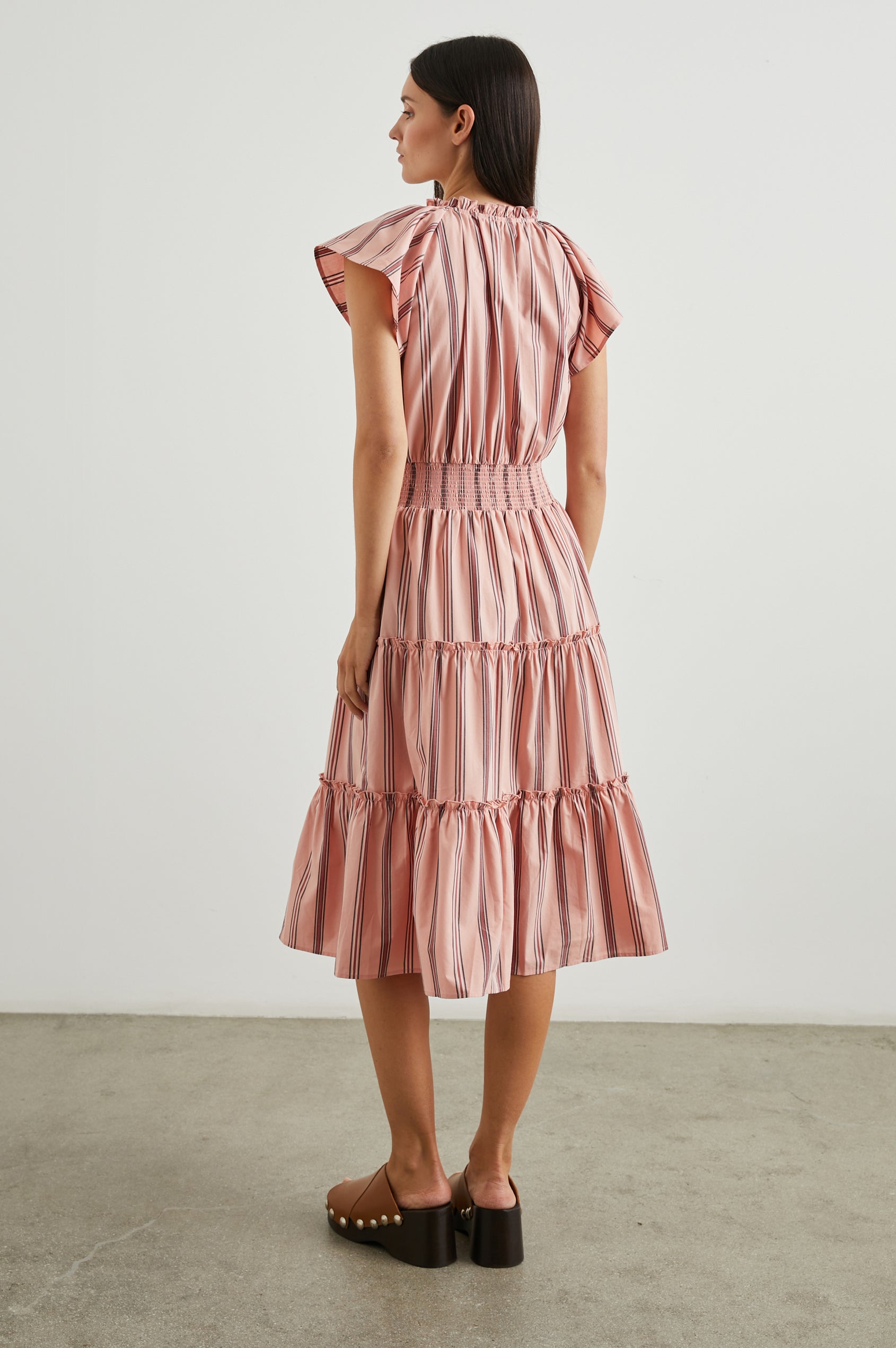 Amellia Short-Sleeve Midi Dress with Smocked Waist and Collar, V Neck, and a Tiered Skirt in Coral Navy Stripe Colorway, Vertical Coral and Navy Stripes on Peach - Back View Featured on Model