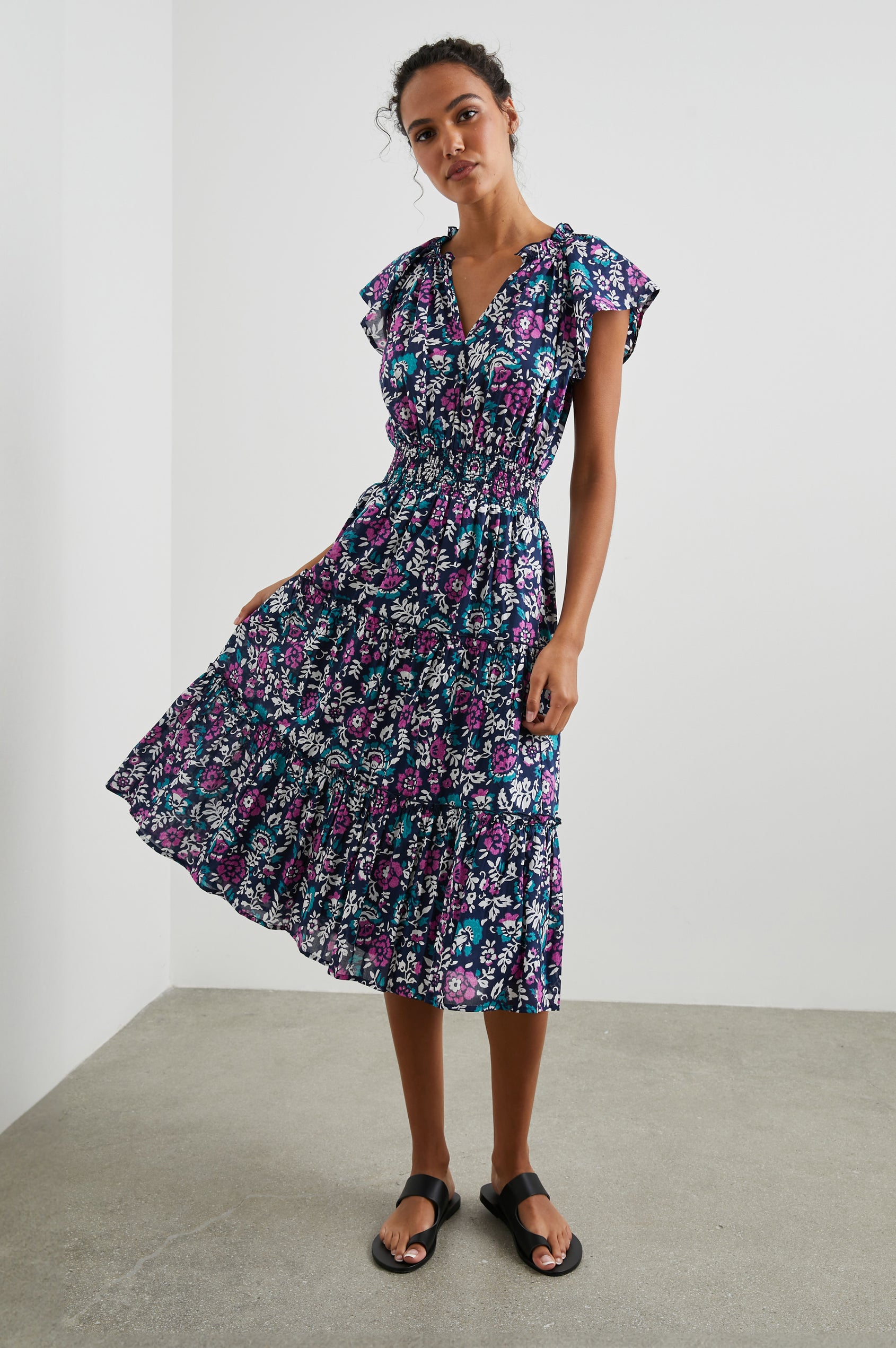 Amellia Short-Sleeve Midi Dress with Smocked Waist and Collar, V Neck, and a Tiered Skirt in Woodblock Floral Colorway, Flowers in Purples, Greens and White on Navy - Front Full Body View Featured on Model