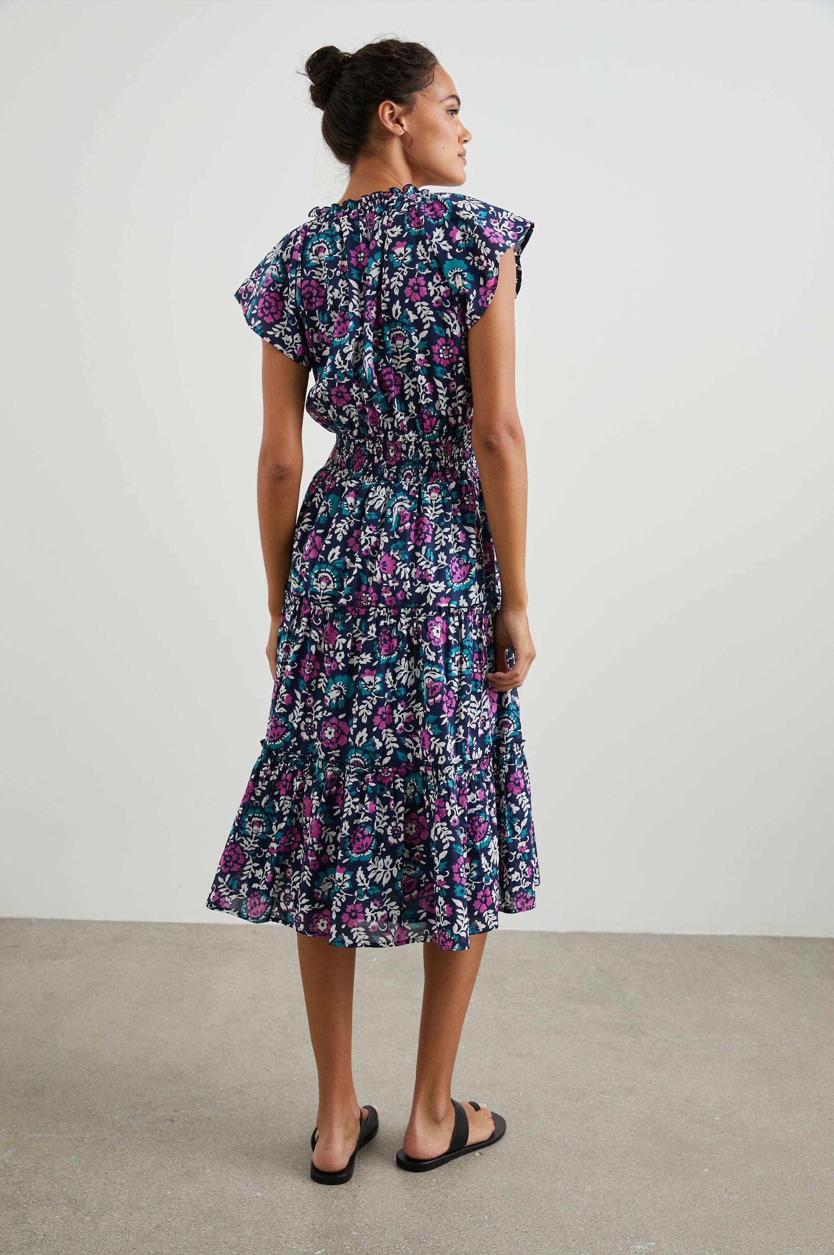 Amellia Short-Sleeve Midi Dress with Smocked Waist and Collar, V Neck, and a Tiered Skirt in Woodblock Floral Colorway, Flowers in Purples, Greens and White on Navy - Back Full Body View Featured on Model