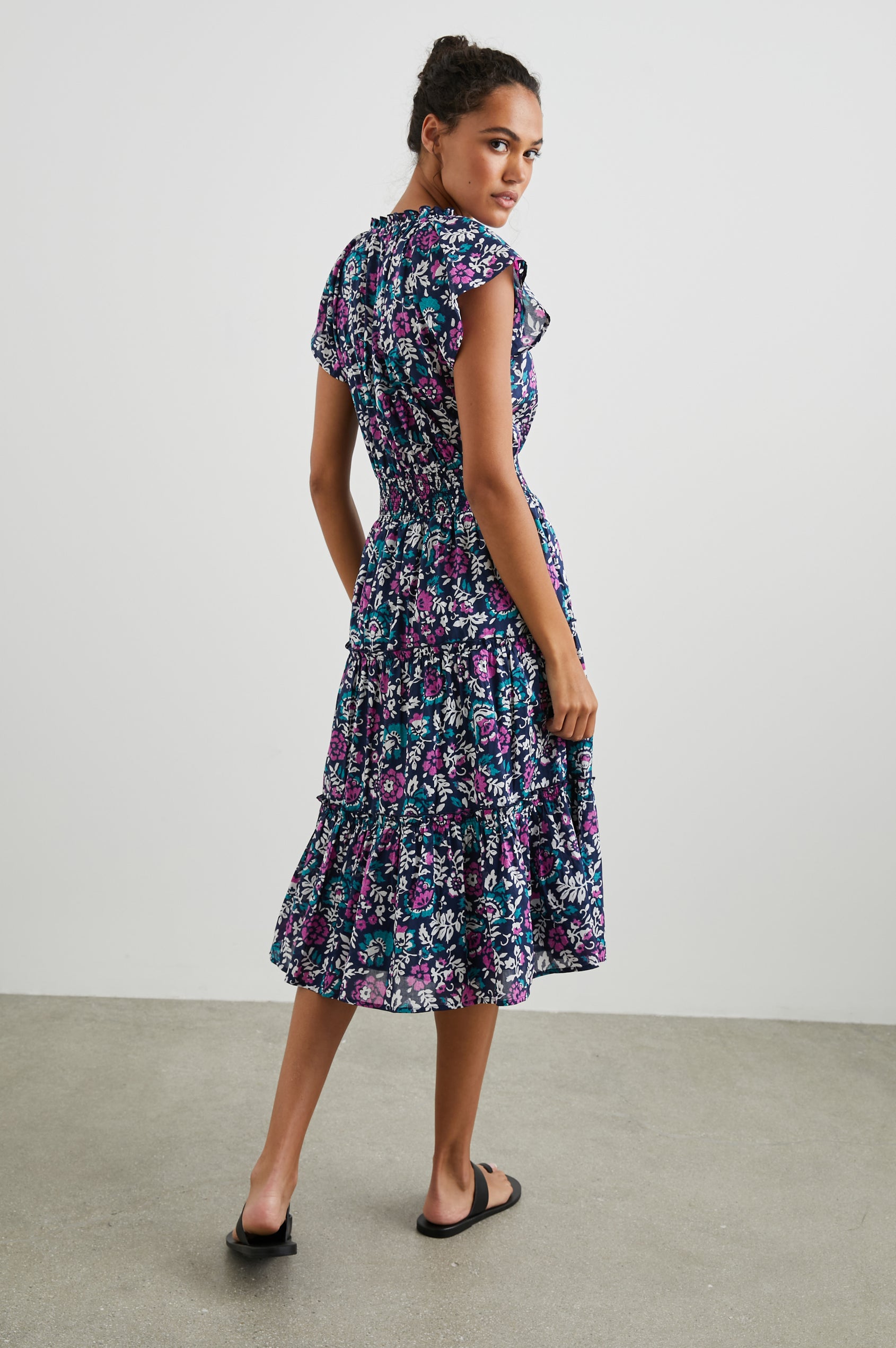 Amellia Short-Sleeve Midi Dress with Smocked Waist and Collar, V Neck, and a Tiered Skirt in Woodblock Floral Colorway, Flowers in Purples, Greens and White on Navy - Back Full Body View Featured on Model