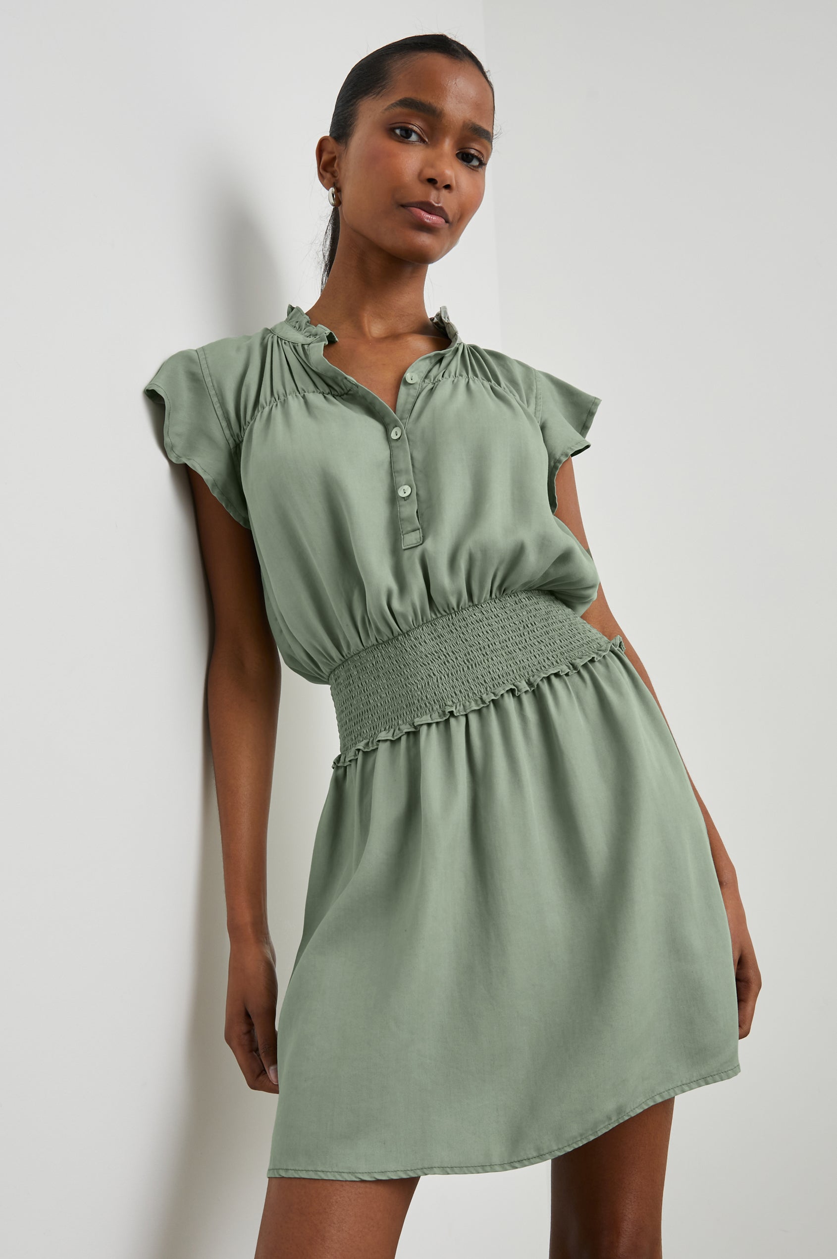 Amina Short Sleeve Mini Dress with Flutter Sleeves, a Ruffled Collar with Ruching, a Button Placket, and a Shirred Waist in Sage Denim Colorway - Front View Featured on Model 