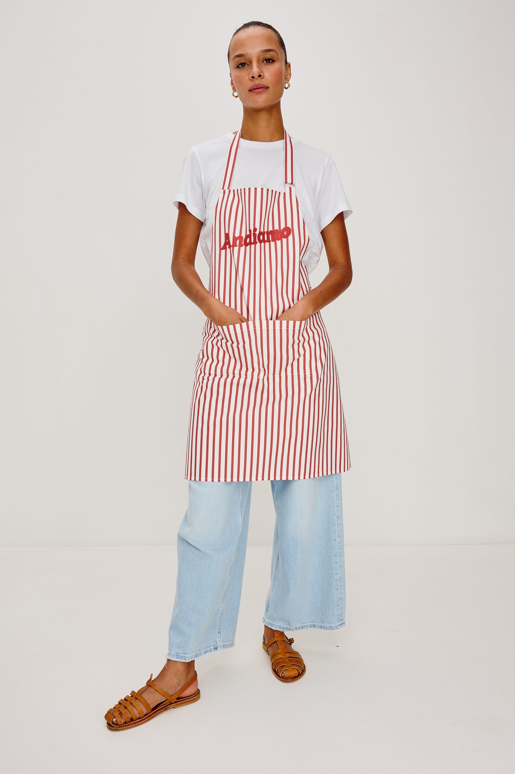 Andiamo Apron in Ravello Stripe with adjustable neck straps, dual front pockets and 'Andiamo' expression on the chest. Front view on model, hands in pockets