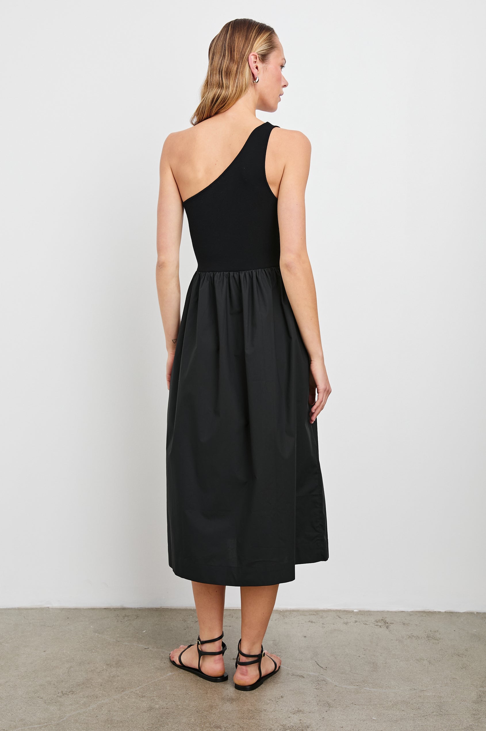 Anita Sleeveless, Midi Dress with an Asymmetrical Neckline and a Cinched Waist in Black Colorway - Back Full Body View Featured on Model