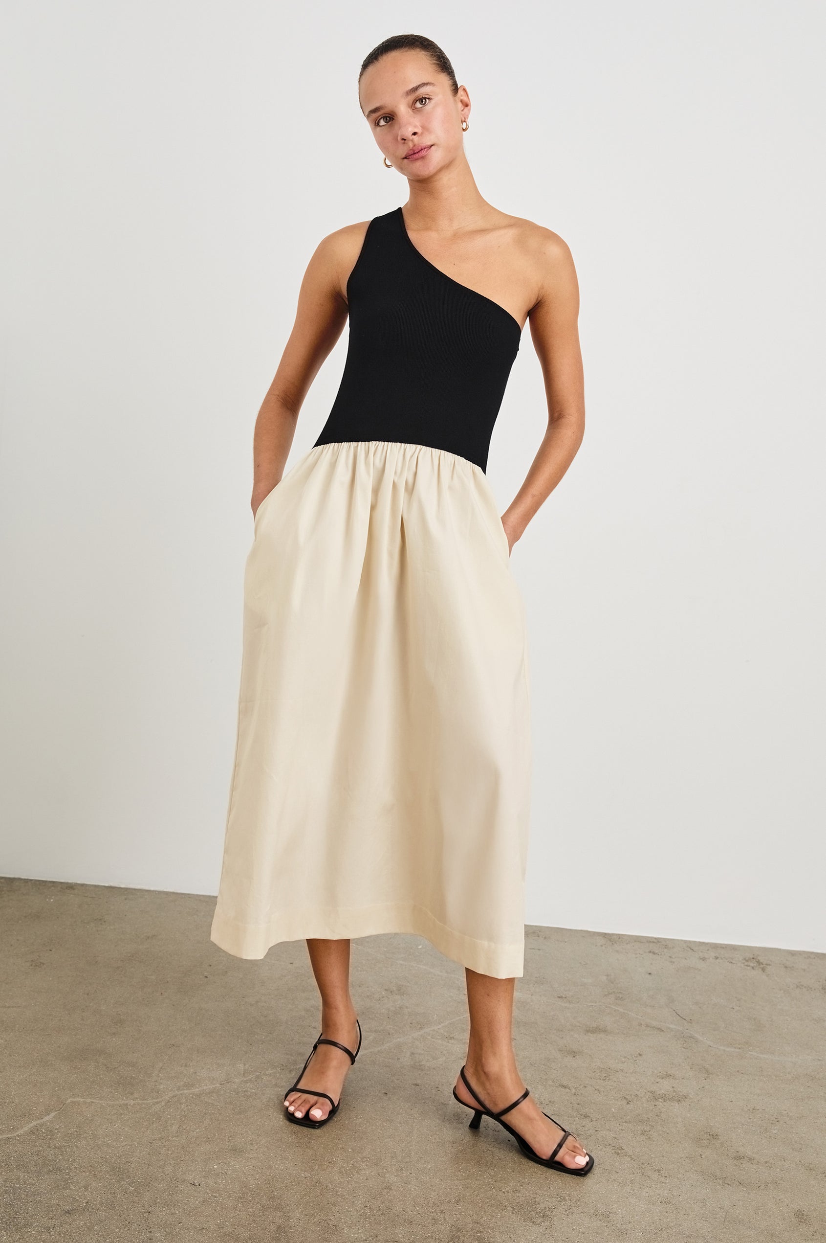 Anita Dress with Black asymmetrical bodice and ivory poplin midi skirt - full front body with hands in pockets, on model