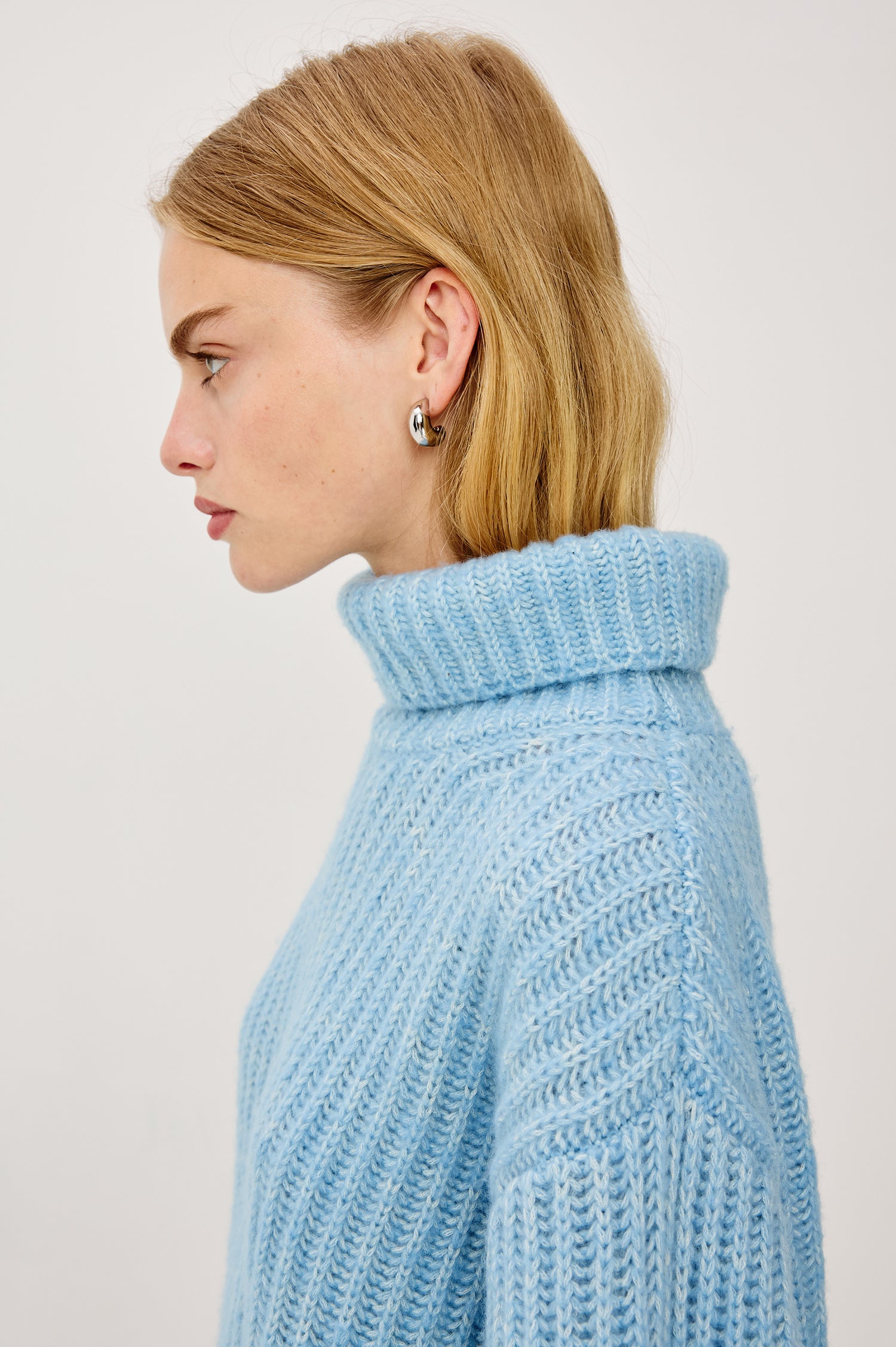 Anja Turtleneck Sweater in Soft Ribbed Knit With Relaxed Fit, High Low Hem, and Long Sleeves in Light Blue Colorway - Upper Body Side View Featured on Model