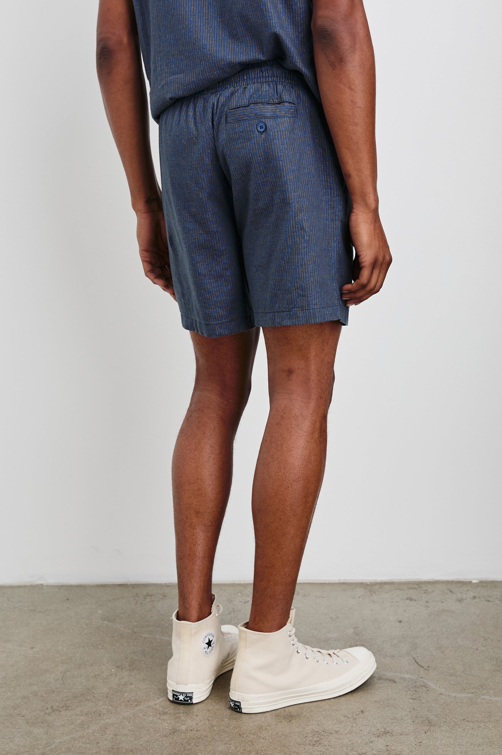 Aries Shorts with a Drawstring Waist, Two Front Pockets and a Buttoned Back Patch Pocket in Navy Cedar Vertical Colorway, with Thin Vertical Cedar Dashes on Navy - Back View Featured on Model