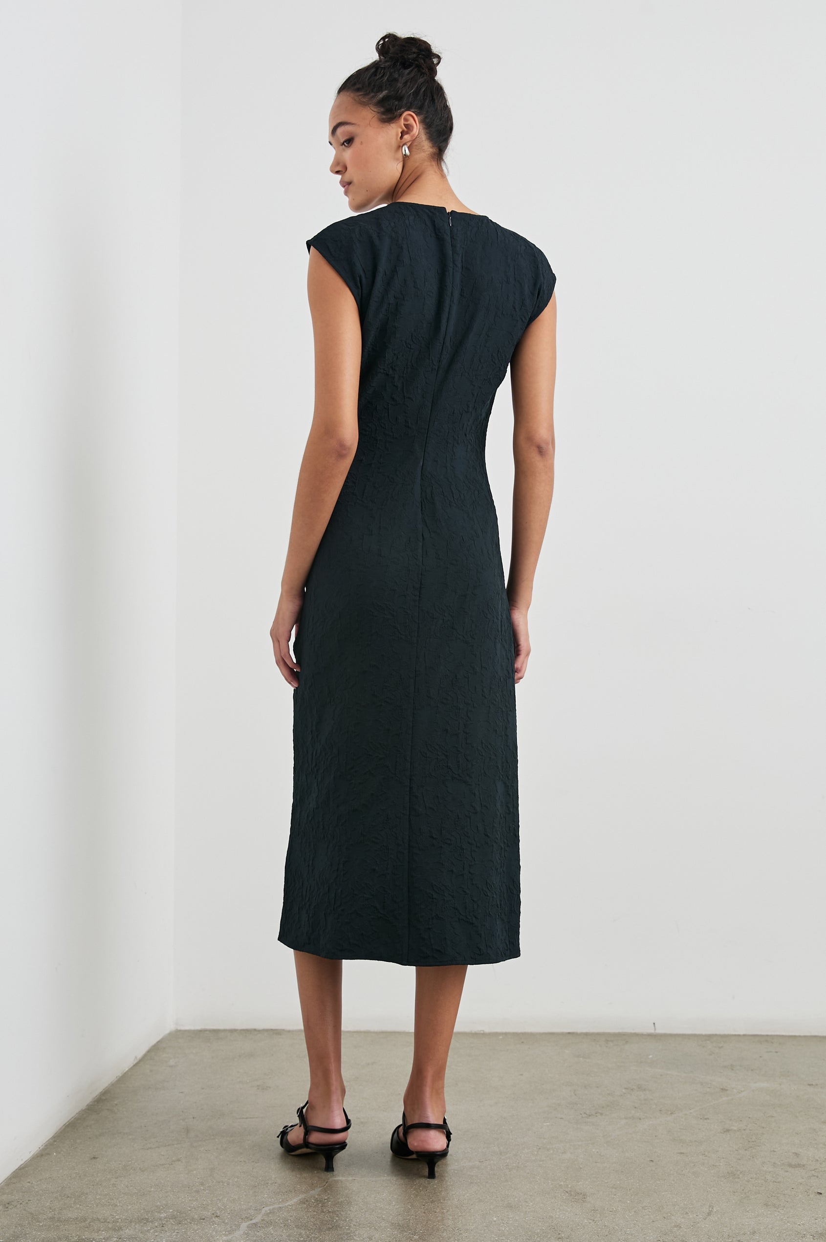 Auren Midi Dress with Cap Sleeves, a Deep V Neck, a Mid-Thigh Side Slit and Ruching from the V Neck to the Slit with a Drawcord at the Slit in Black Jacquard Colorway - Back Full Body View Featured on Model 