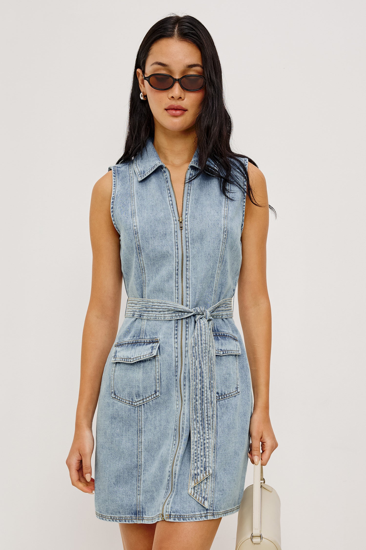 Aurora Sleeveless Mini Dress in TENCELâ„¢Denim With Collar Front Exposed Zipper Adjustable Belted Ties Side Flap Pockets in Faded Indigo Colorway - Upper Body Front View Featured on Model