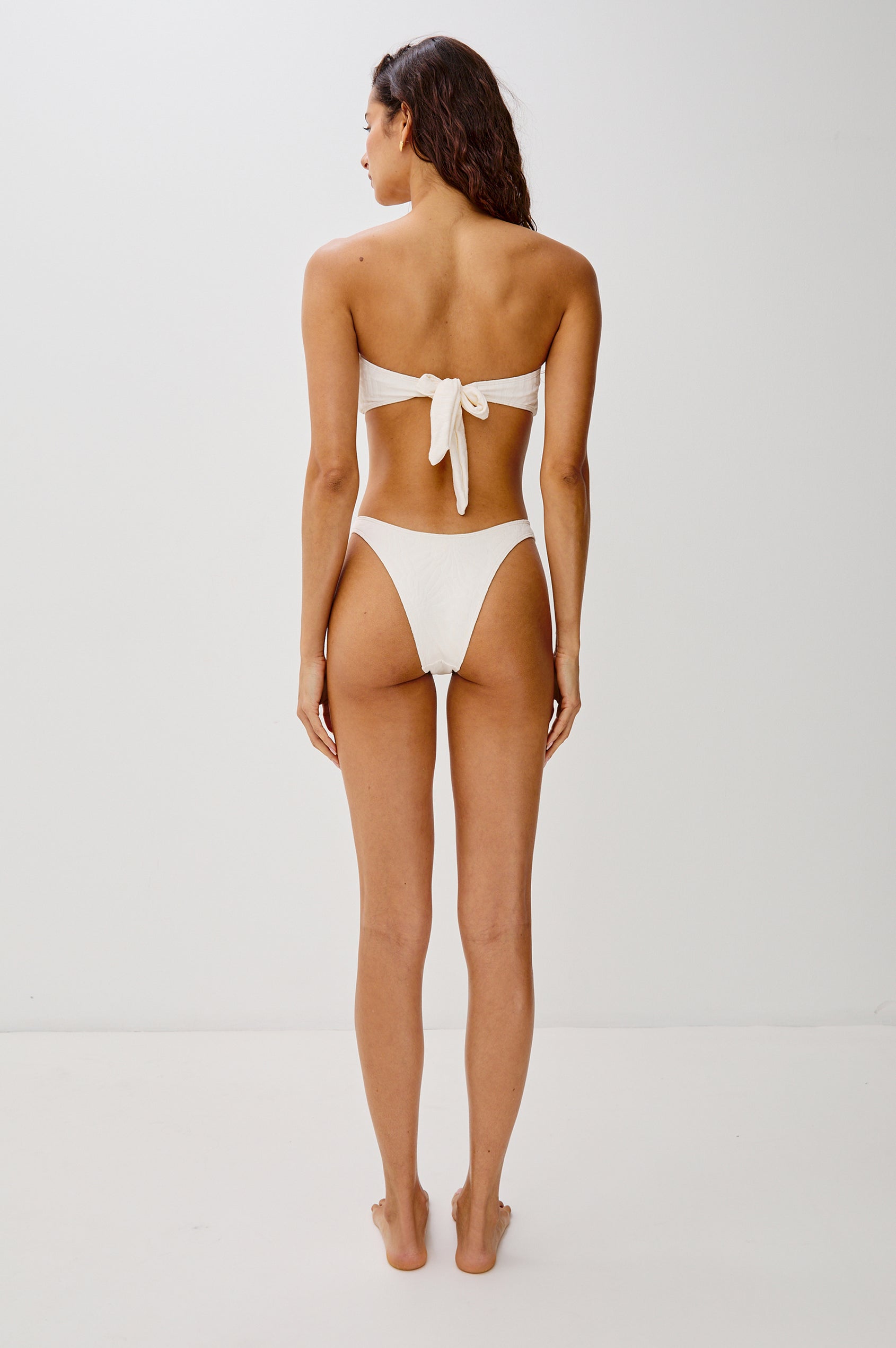 Rocky French Cut Low Rise Bikini Bottom with Spiral Hardware, Fossils Texture and Provides Classic Coverage in Cream Colorway. Full Body Back View Shown on Model.