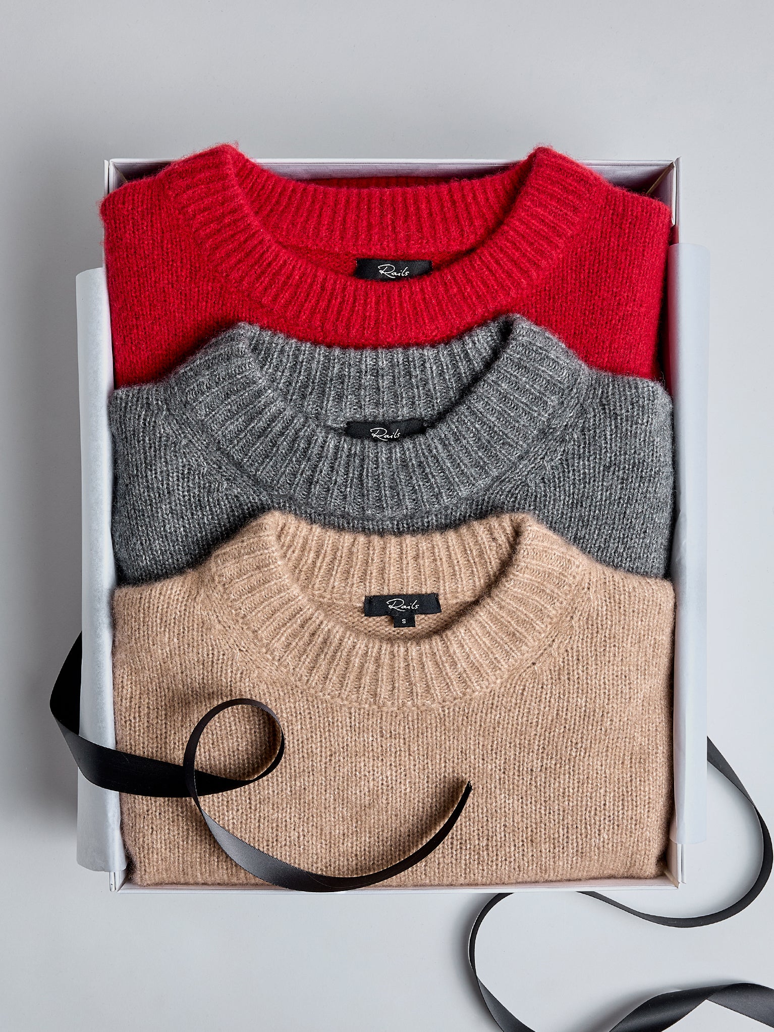 EDITORIAL IMAGE OF MULTIPLE CASHMERE SWEATERS FOLDED IN A GIFT BOX TOGETHER