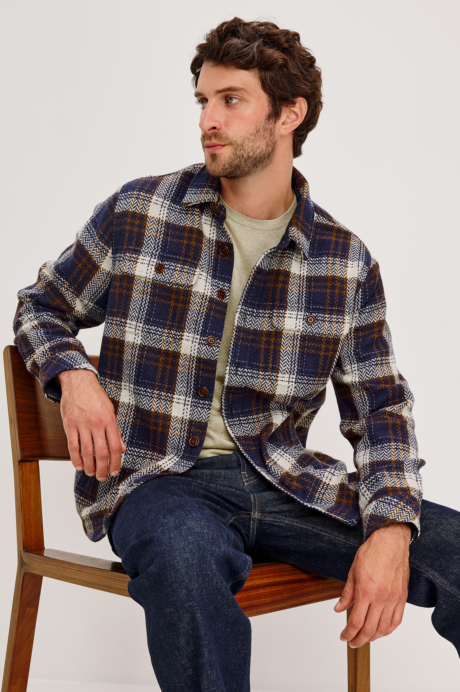 The Berkshire is a plaid shirt jacket with two chest pockets button front and collar in Navy Umber Cream colorway. Front seated view featured on model.