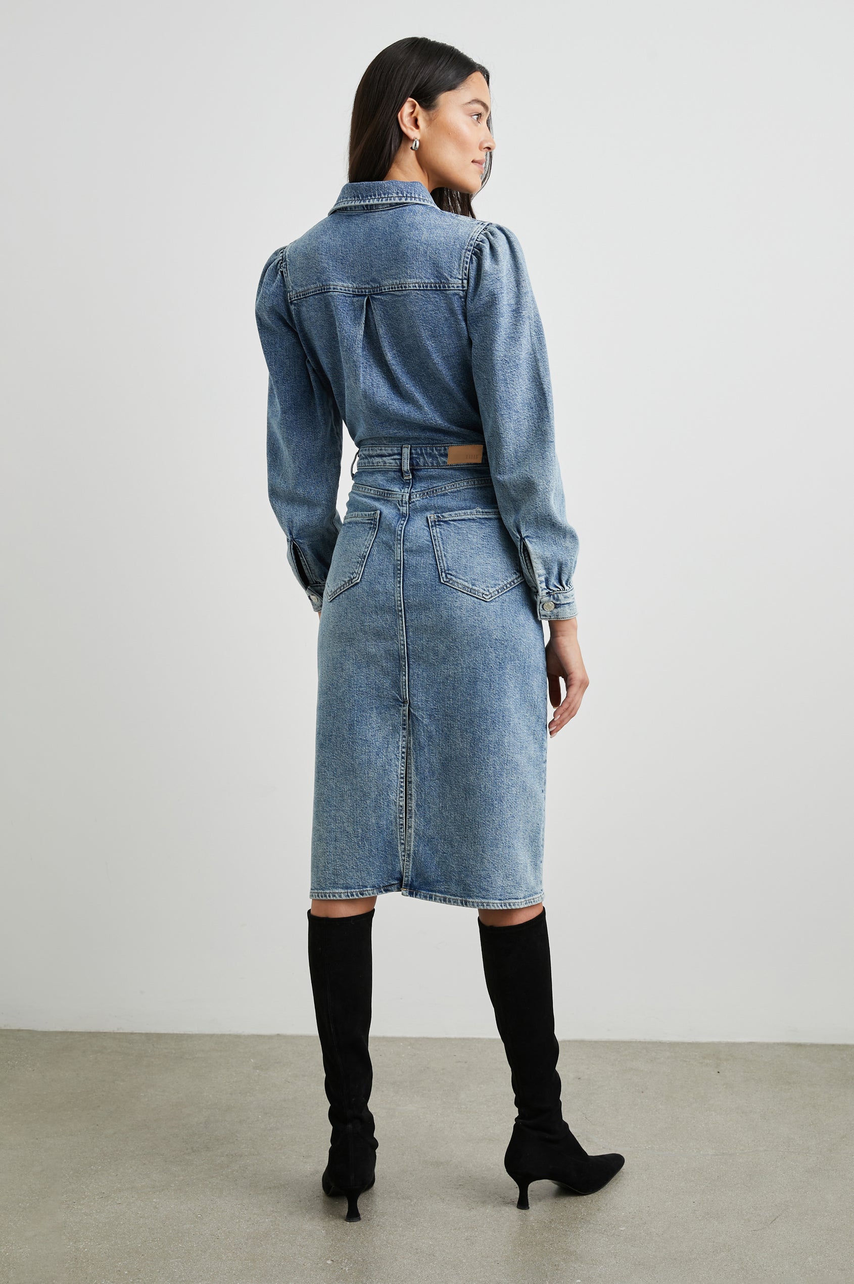 Beverly Long Sleeve Denim Knee Dress with a Back Vent, Belt Loops, a Button and Zipper Closure for the Skirt and Button Closure on the Bodice, a Collar, two Front Pockets plus a Coin Pocket and Two Back Patch Pockets in West Coast Colorway, a Blue - Back Full Body View Featured on Model