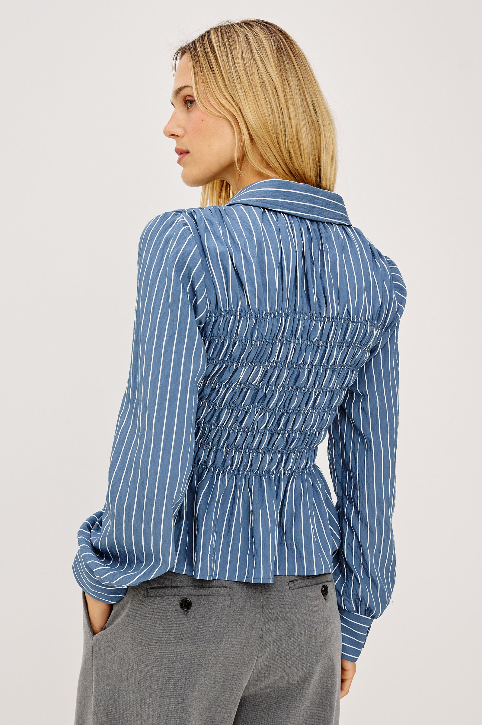 Bradshaw Shirt in Cotton Poplin With Button-Up Front, Collar, Smocked Body, Peplum Hem, and Bishop Sleeves in Washed Indigo Stripe Colorway - Upper Body Back View Featured on Model