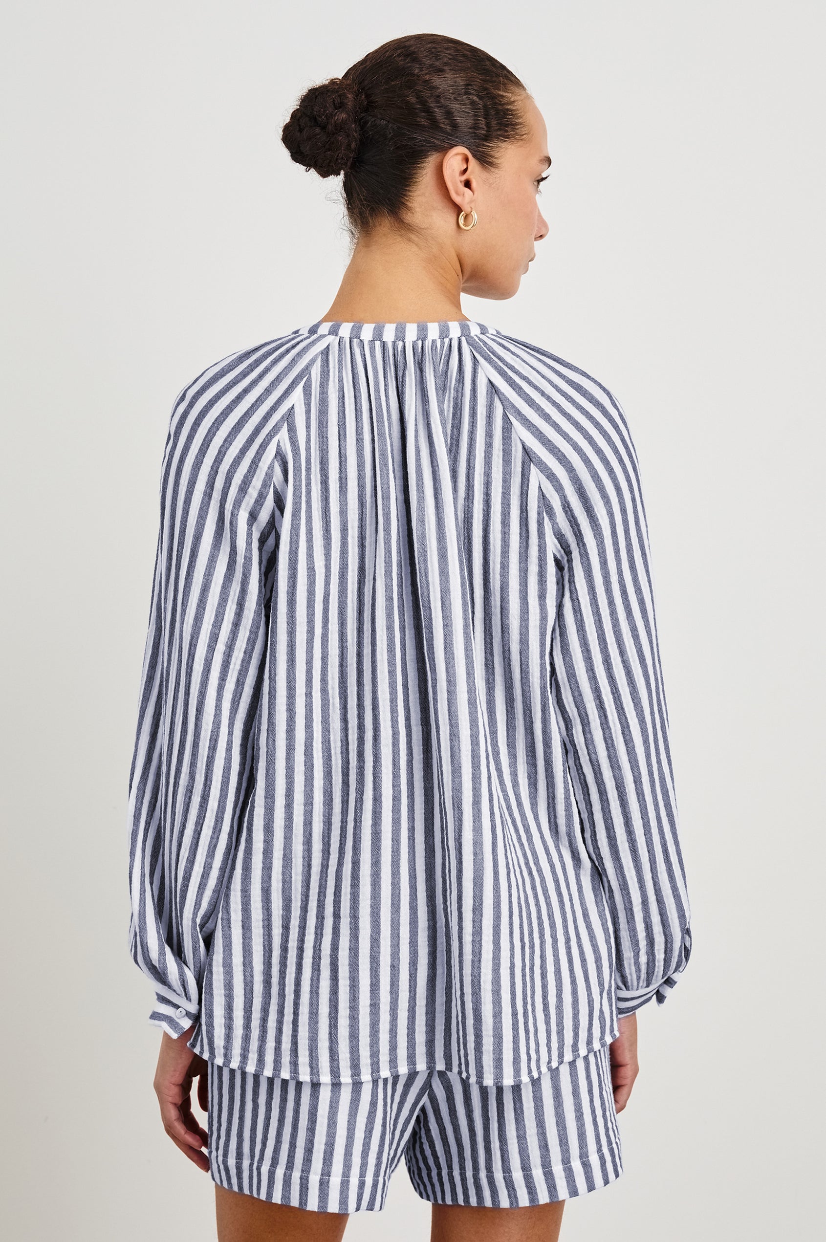 Back view of model wearing our Brielle Top, an airy style with a mandarin collar, raglan sleeves and front ties. Print is a blue and white vertical stripe.  Styled with matching striped shorts. 