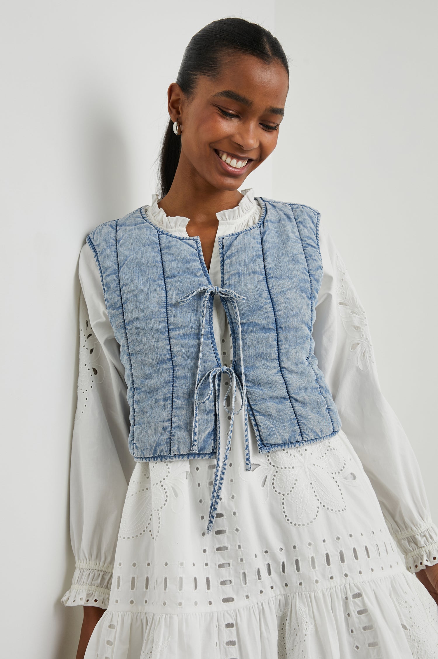 Bronte Sleeveless Cropped Denim Top with Front Tie Closure and Vertical Seams in Medium Cloud Wash Colorway - Front View Featured on Model, Layered Over a Second Shirt 