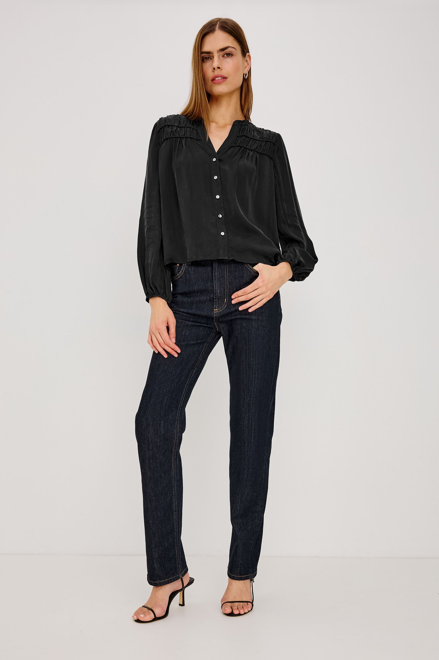 Cadence Shirt in Silky Fabric With Cutaway V-Neck, Shirred Yoke, Front Button Placket, and Slight Puff Long Sleeves and Elastic Cuffs in Black Colorway - Full Body Front View Featured on Model
