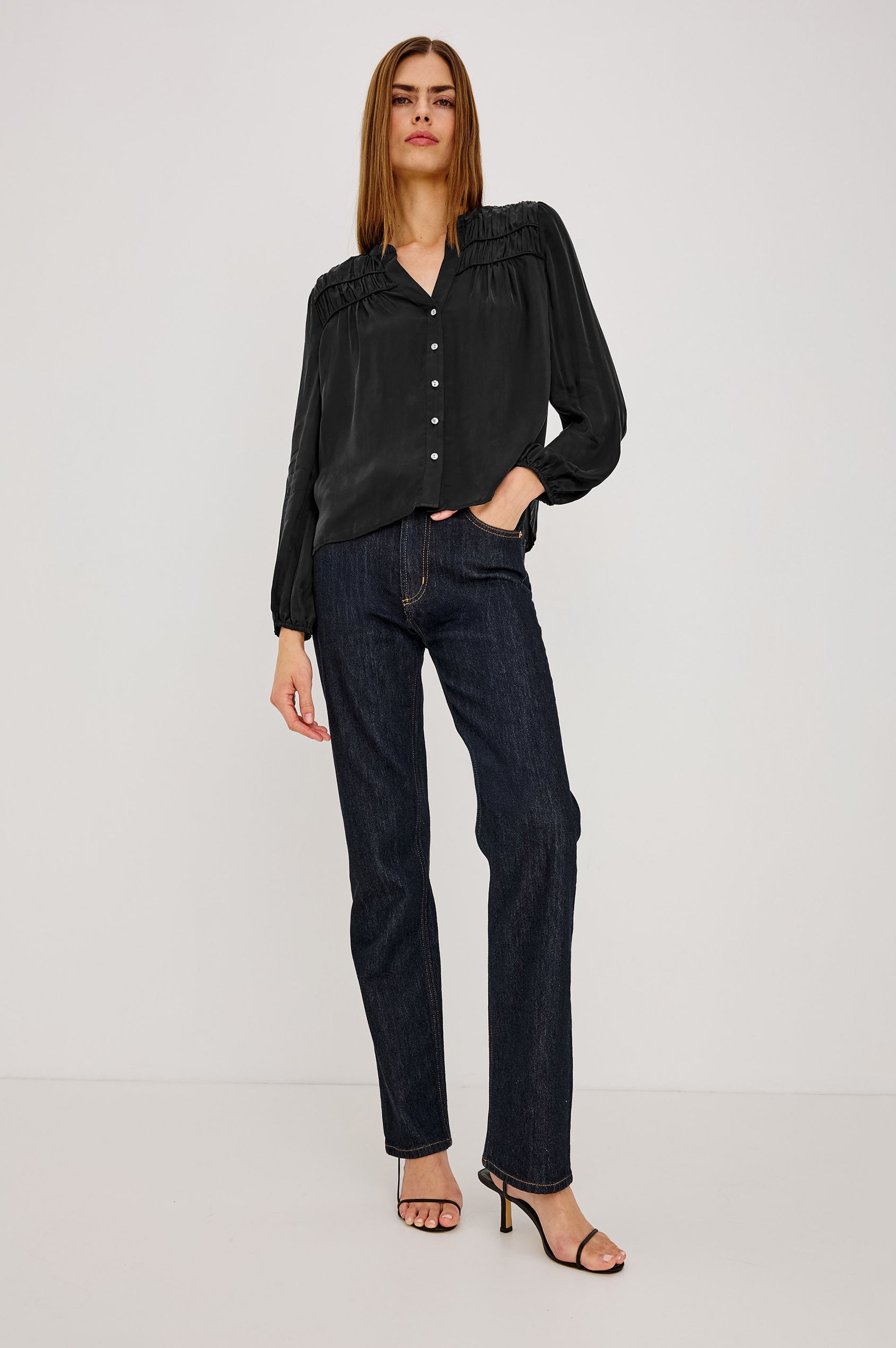Cadence Shirt in Silky Fabric With Cutaway V-Neck, Shirred Yoke, Front Button Placket, and Slight Puff Long Sleeves and Elastic Cuffs in Black Colorway - Full Body Front View Featured on Model