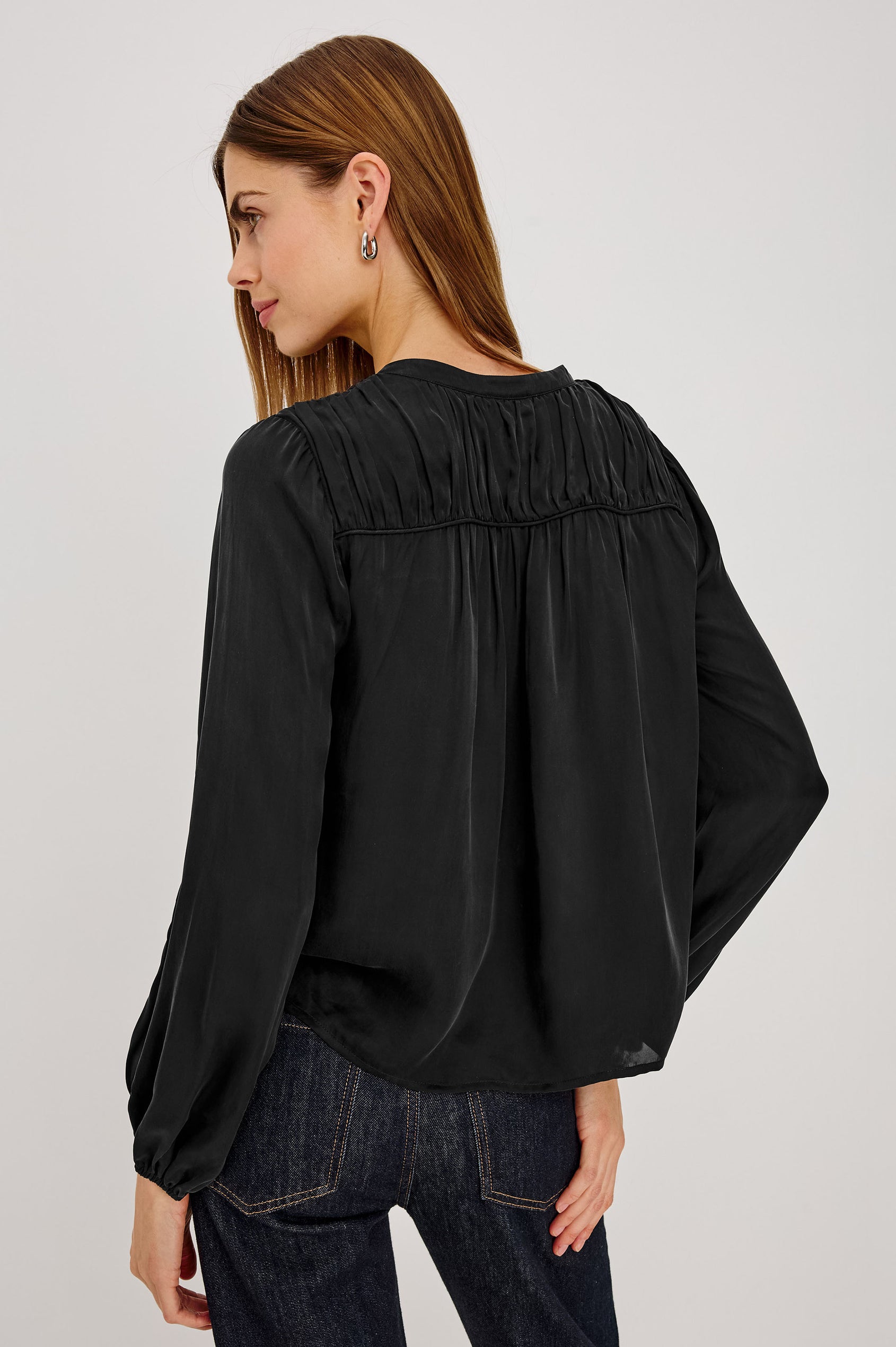 Cadence Shirt in Silky Fabric With Cutaway V-Neck, Shirred Yoke, Front Button Placket, and Slight Puff Long Sleeves and Elastic Cuffs in Black Colorway - Upper Body Back View Featured on Model