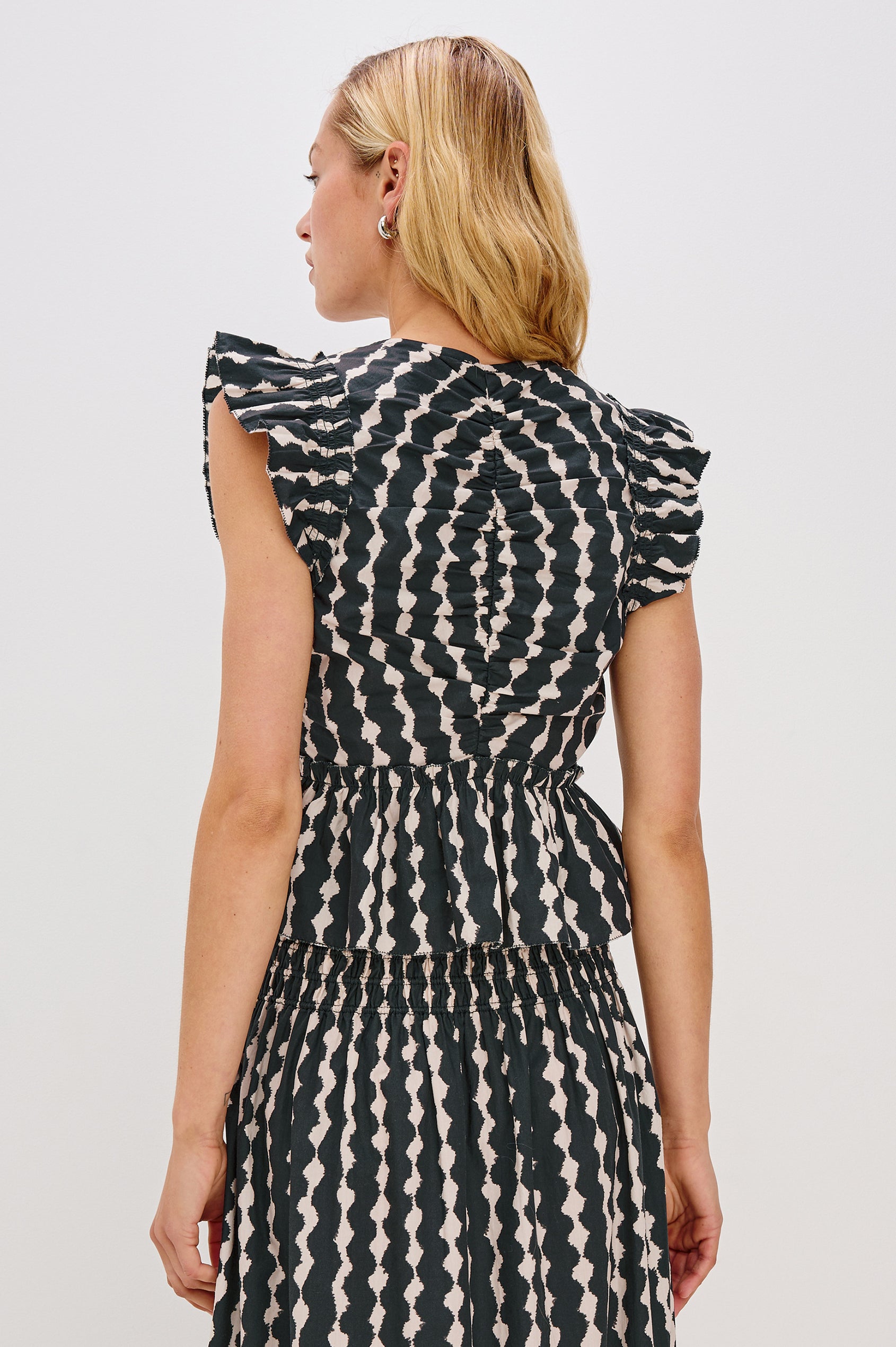 Cali short sleeve top with center front ruching, flutter sleeves, and a ruffle hem in Painted Noir colorway - back view on model