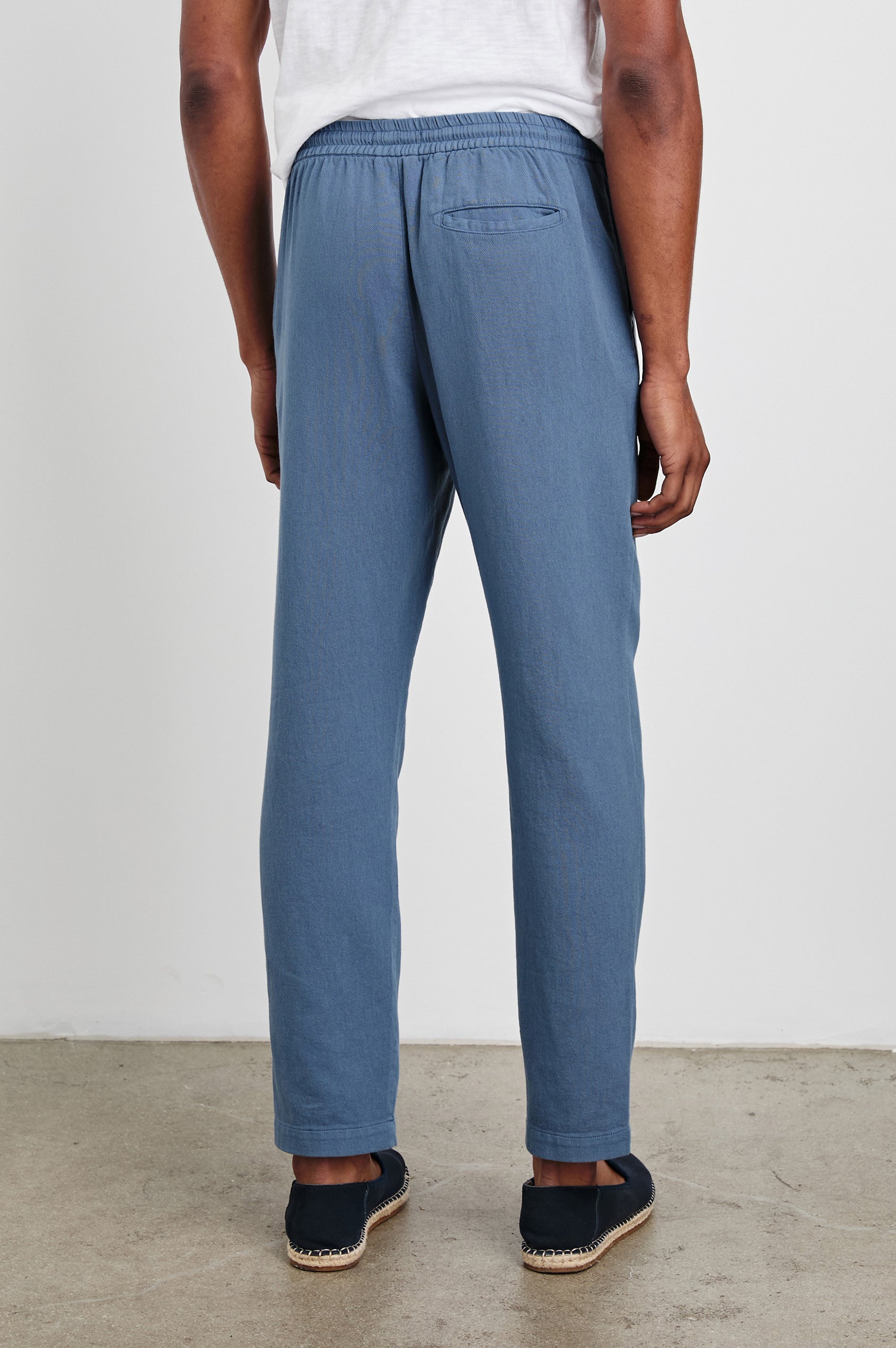 Callum Pants with a Drawstring Waist, Two Front Pockets and a Back Patch Pocket in Washed Blue Colorway - Back Full Body View Featured on Model.