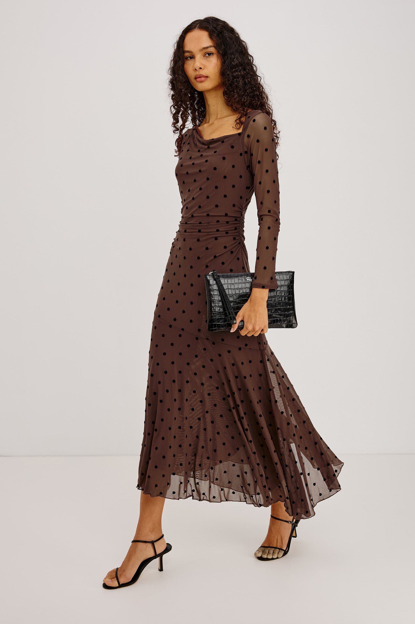 Cambria Midi Dress in Semi-Sheer Stretch Mesh With Velvet Polka Dots, Self-Lined Body, Asymmetric Cowl Neckline, Ruched Side Waist, and Softly Flared Skirt in Chocolate Polka Dot Colorway - Full Body Front View Featured on Model