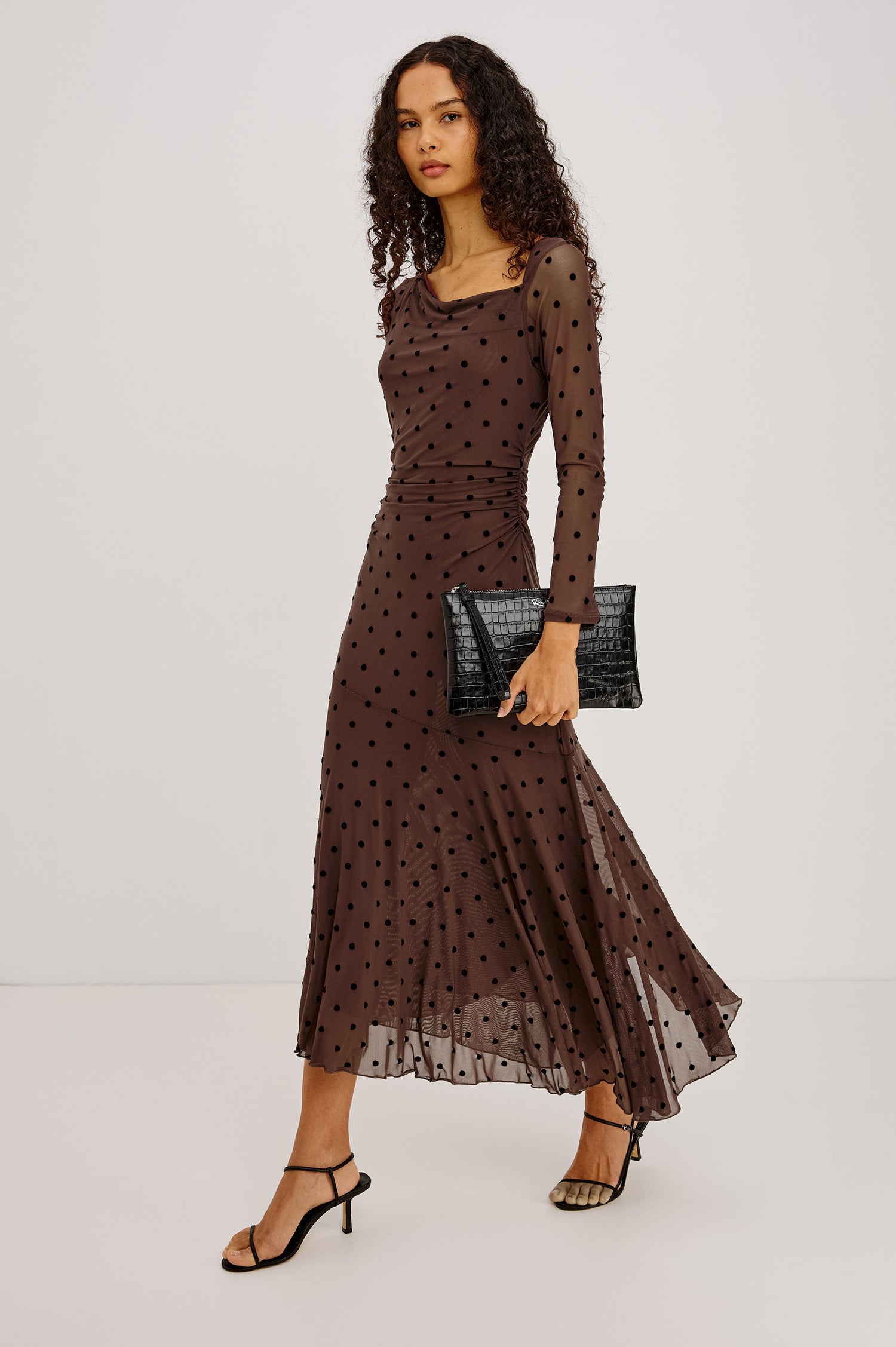 Cambria Midi Dress in Semi-Sheer Stretch Mesh With Velvet Polka Dots, Self-Lined Body, Asymmetric Cowl Neckline, Ruched Side Waist, and Softly Flared Skirt in Chocolate Polka Dot Colorway - Full Body Front View Featured on Model