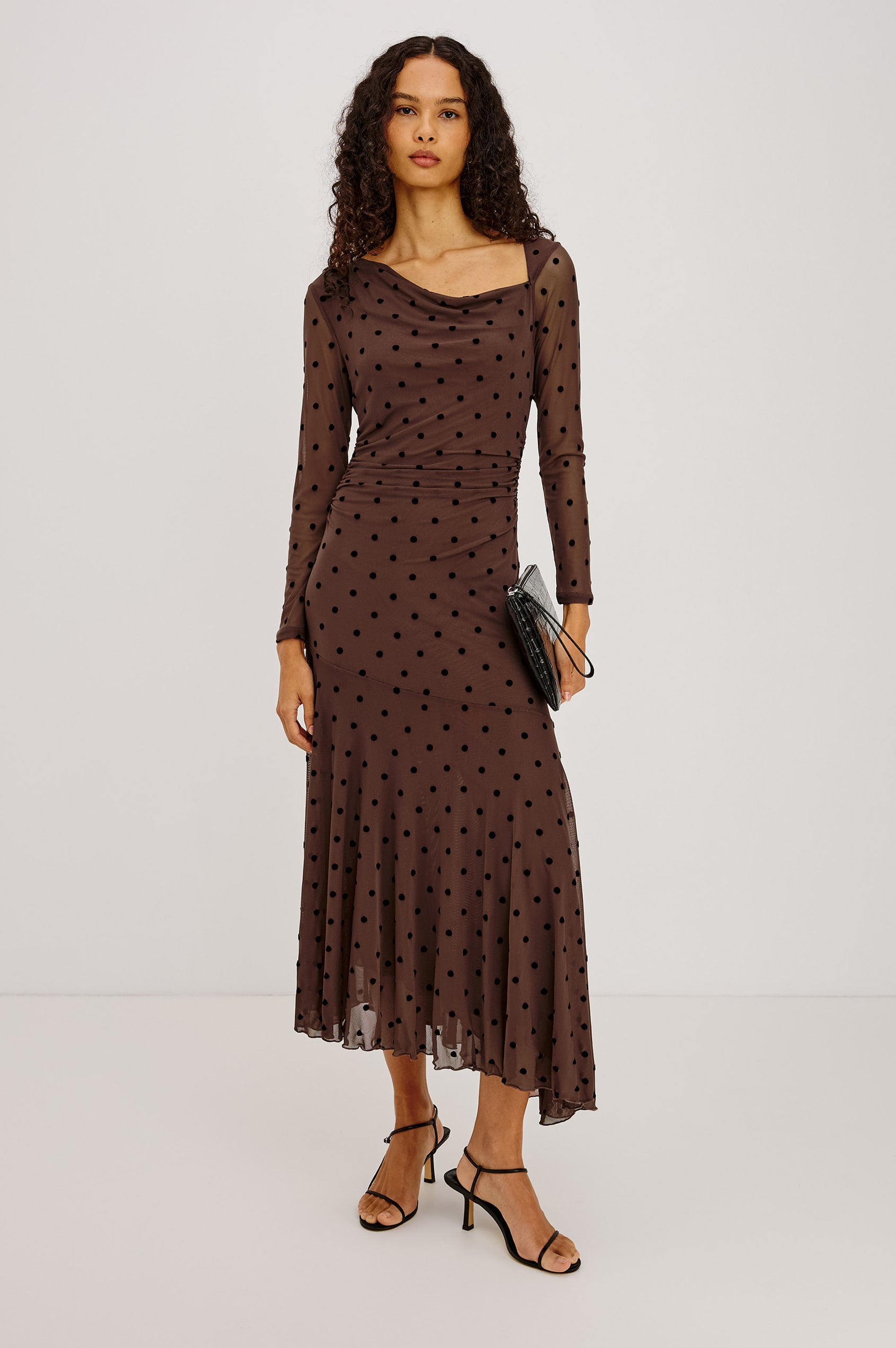 Cambria Midi Dress in Semi-Sheer Stretch Mesh With Velvet Polka Dots, Self-Lined Body, Asymmetric Cowl Neckline, Ruched Side Waist, and Softly Flared Skirt in Chocolate Polka Dot Colorway - Full Body Front View Featured on Model
