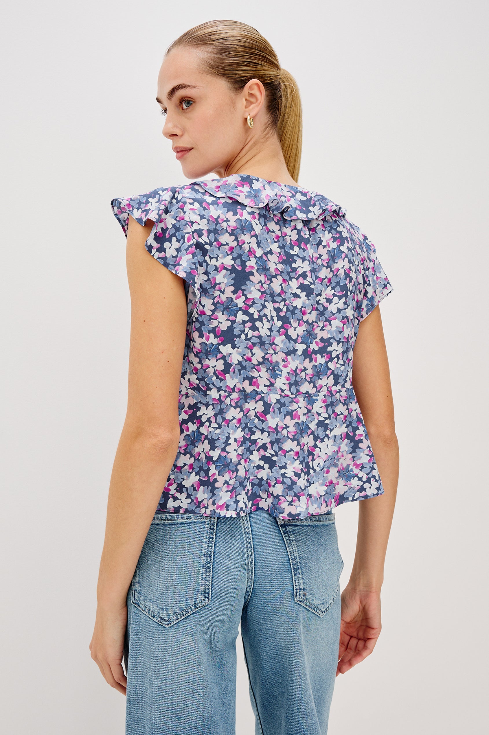 Carmine blouse, a chiffon top with ruffled cap sleeves, ruffles at the v-neckline, a front tie, and empire waist silhouette in Blue Blossom Colorway. Back View Shown on Model.