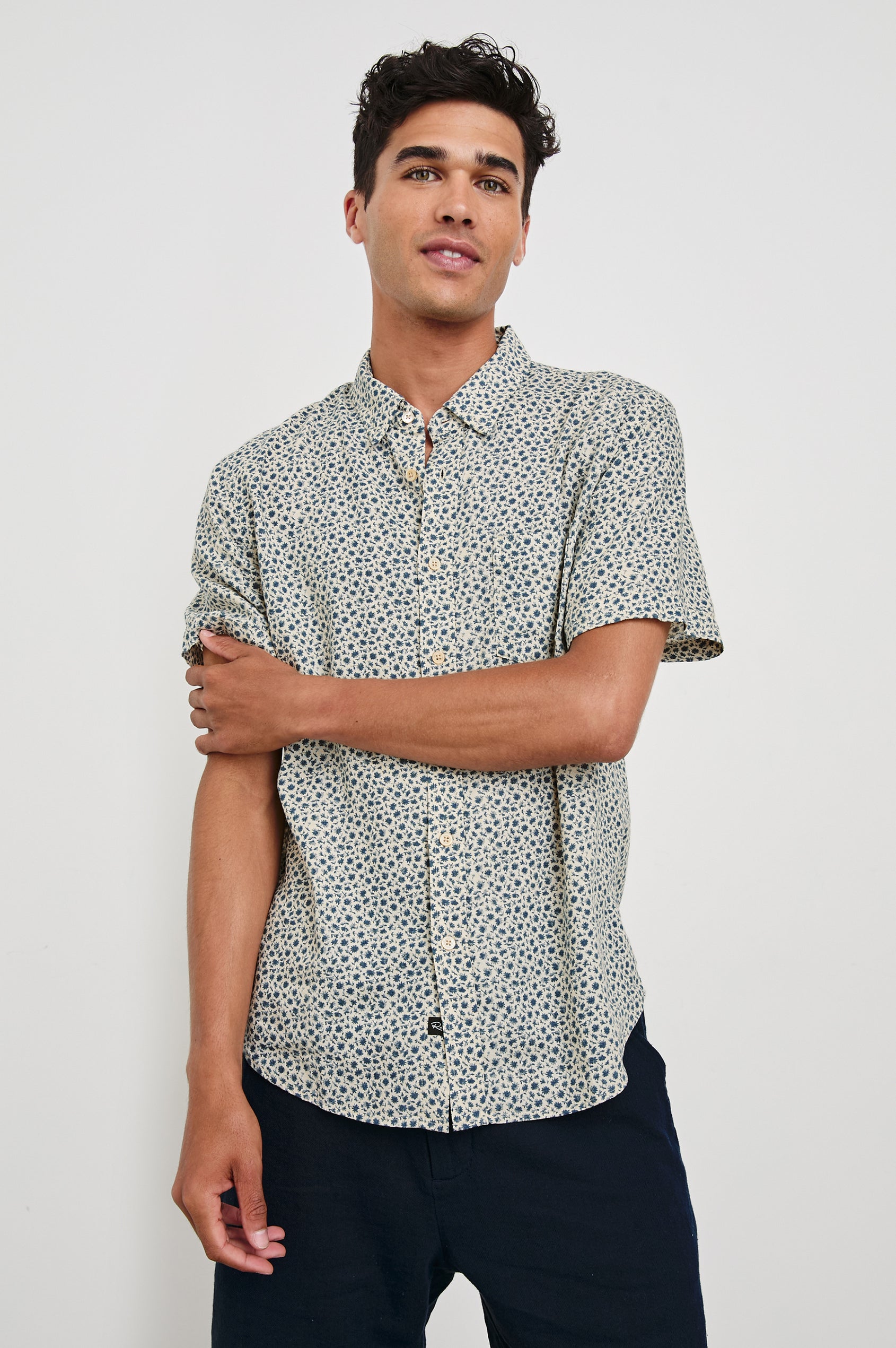 Carson linen short sleeve button down with a collar and blue botanical pattern in Autumn Daisy Ocean - front view on model, arms partially crossed looking straight