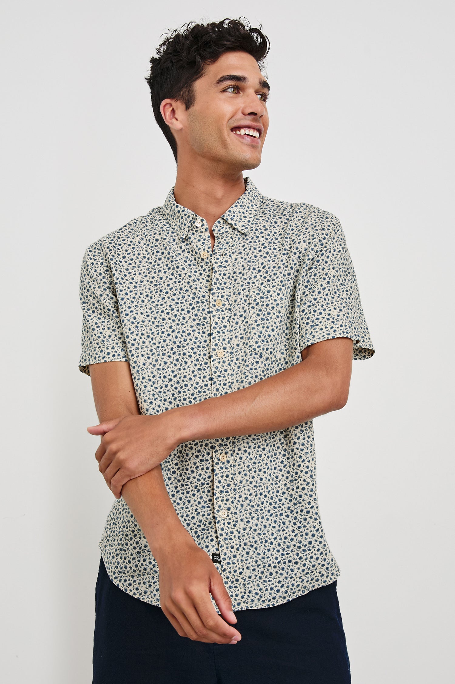 Carson linen short sleeve button down with a collar and blue botanical pattern in Autumn Daisy Ocean - front view on model, arms partially crossed looking away