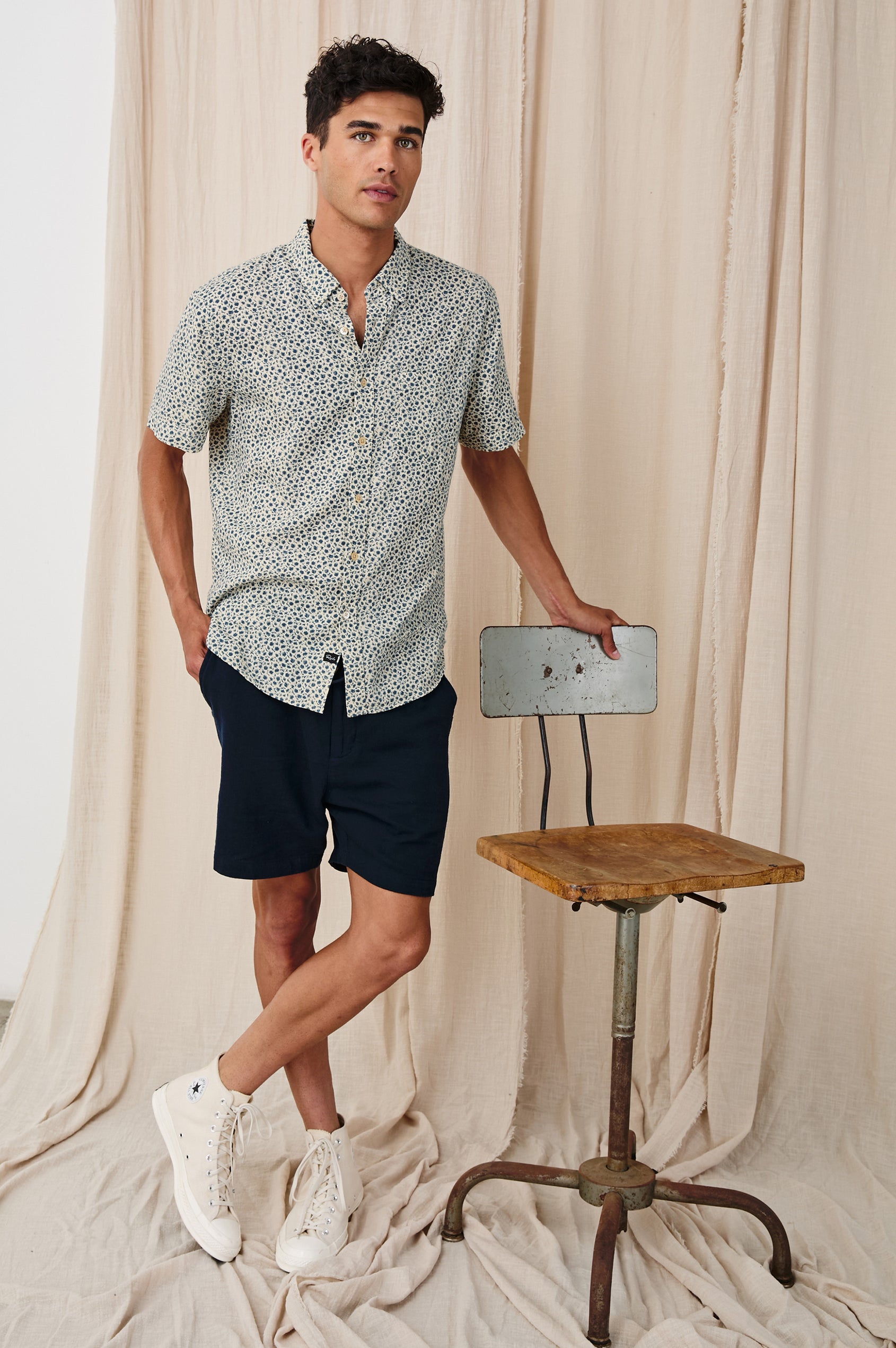 Carson linen short sleeve button down with a collar and blue botanical pattern in Autumn Daisy Ocean - full body front view on model, posing with chair