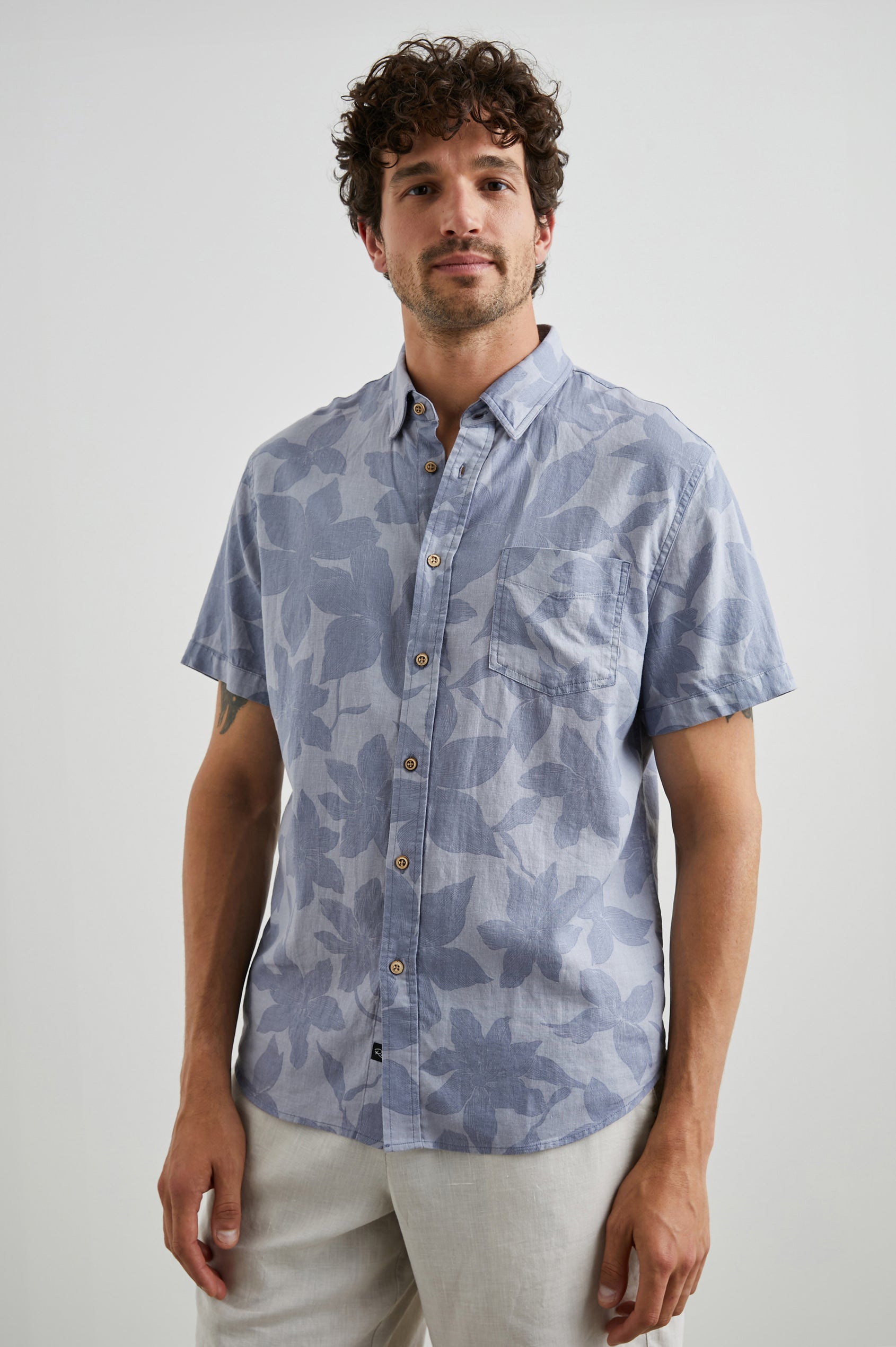 Carson Short Sleeve Button Up with a Chest Patch Pocket in Garden Sands Orchid Colorway, Blue Flowers on Light Blue - Front View Featured on Model