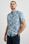 Carson Short Sleeve Button Up with a Chest Patch Pocket in Jungle Garden Reflection Colorway, Flowers and Leaves in Blues on Light Blue - Front View Featured on Model